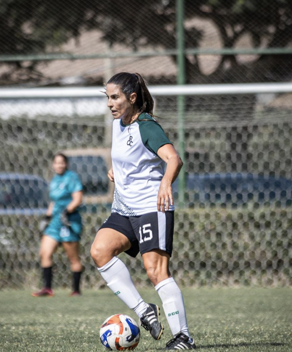 Female soccer player in a white and green jersey with the number 15, on a field with a soccer ball, during a game.