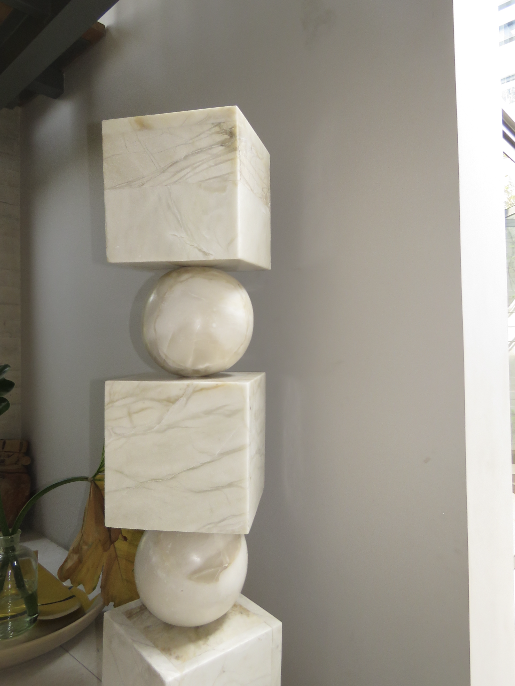 A sculpture with alternating marble cubes and spherical shapes stacked vertically in an indoor setting.