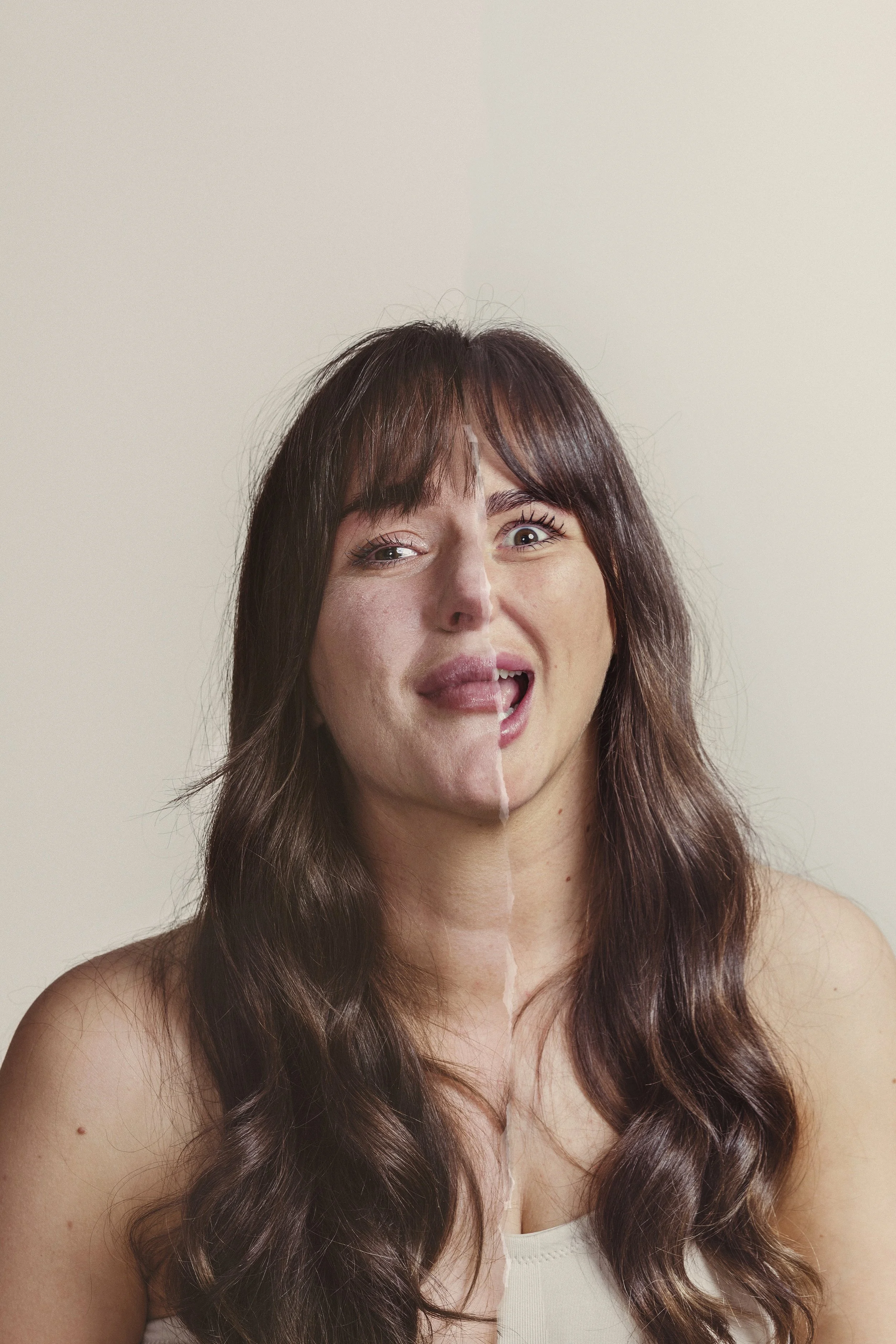 A woman with long, wavy brown hair and light skin making a playful facial expression, with one eye winking and her tongue slightly out, against a plain light background.