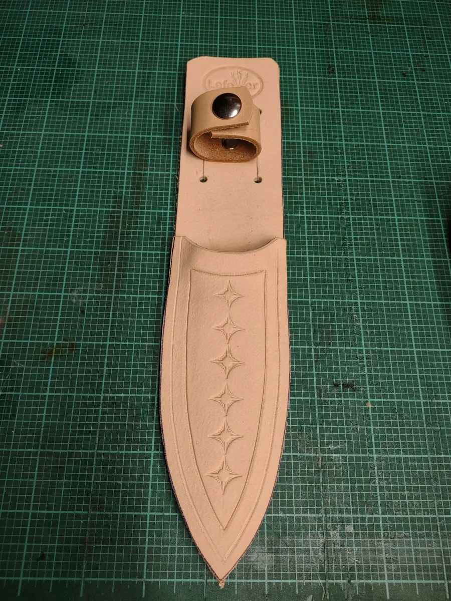 A leather crafting sheath with an embossed star pattern, resting on a green cutting mat.