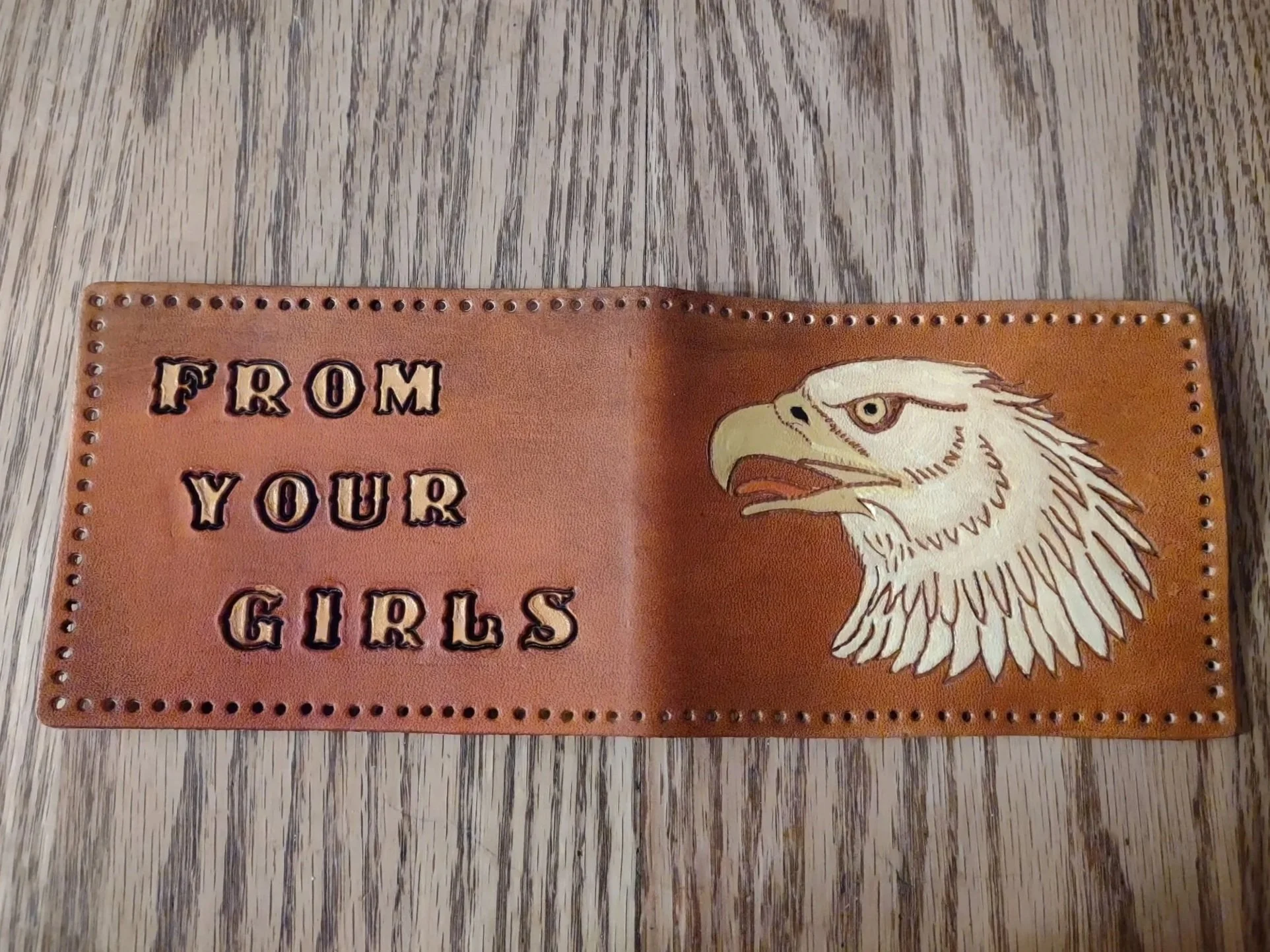 A Leather wallet with the text 'FROM YOUR GIRS' and an image of an eagle's head lying open on a wooden surface.
