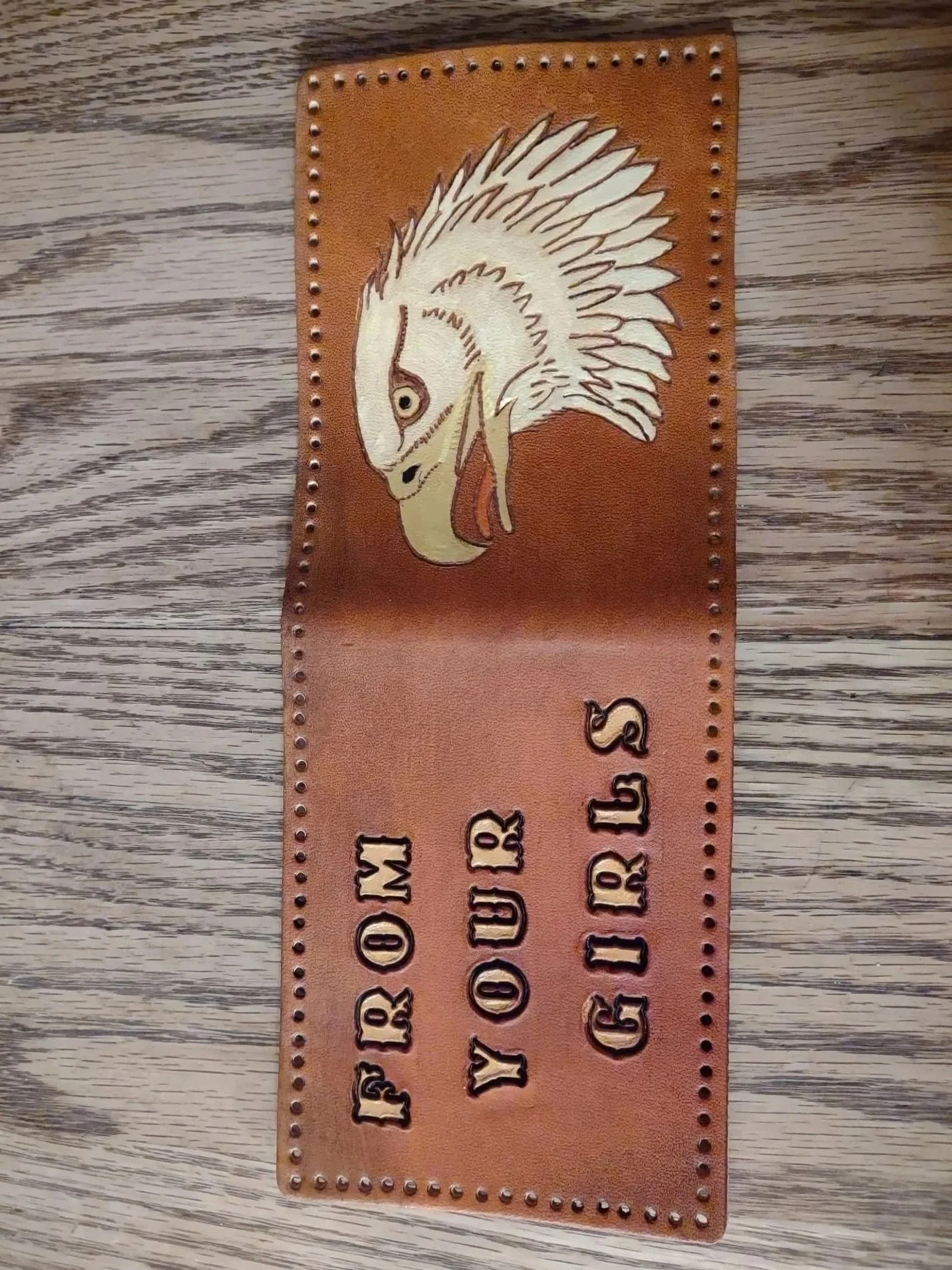 A Leather wallet with the text 'FROM YOUR GIRS' and an image of an eagle's head lying open on a wooden surface.