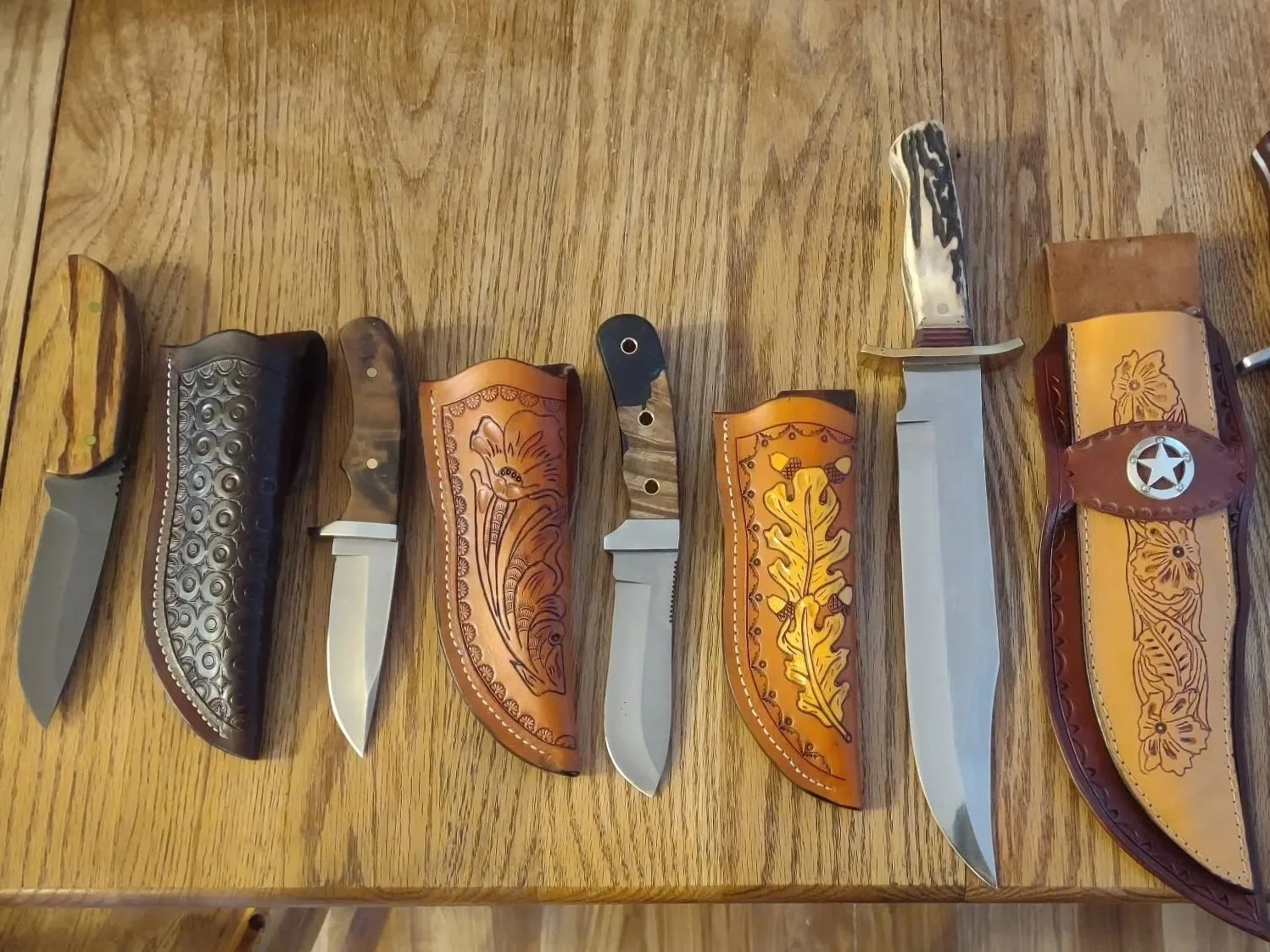 Seven decorative knives with various handles and sheaths laid out on a wooden table.