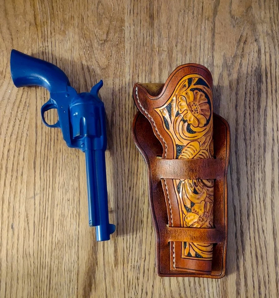 A custom, hand made brown leather holster with an intricate yellow and black floral design.