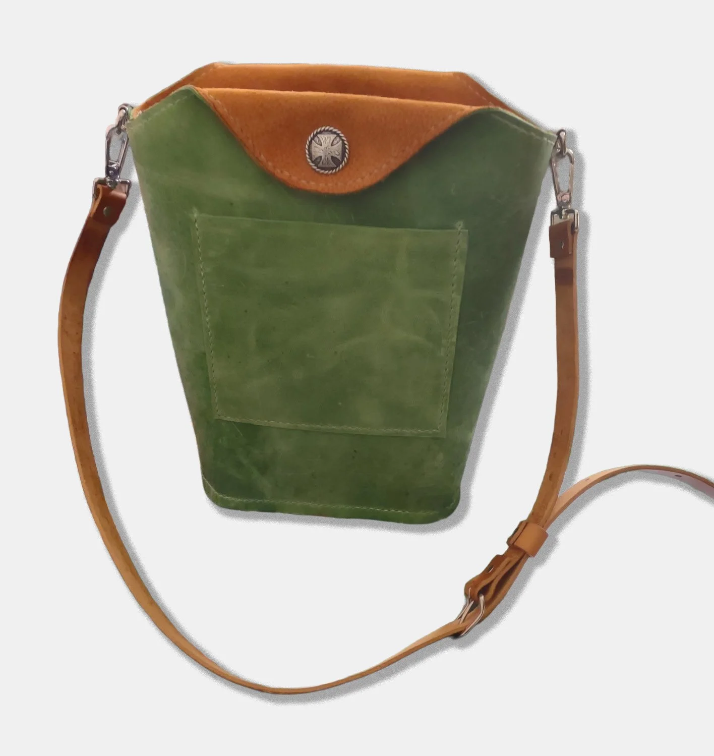 A custom, handmade crossbody bag made of green and brown leather with a front pocket, leather strap, and a silver button with a cross emblem.