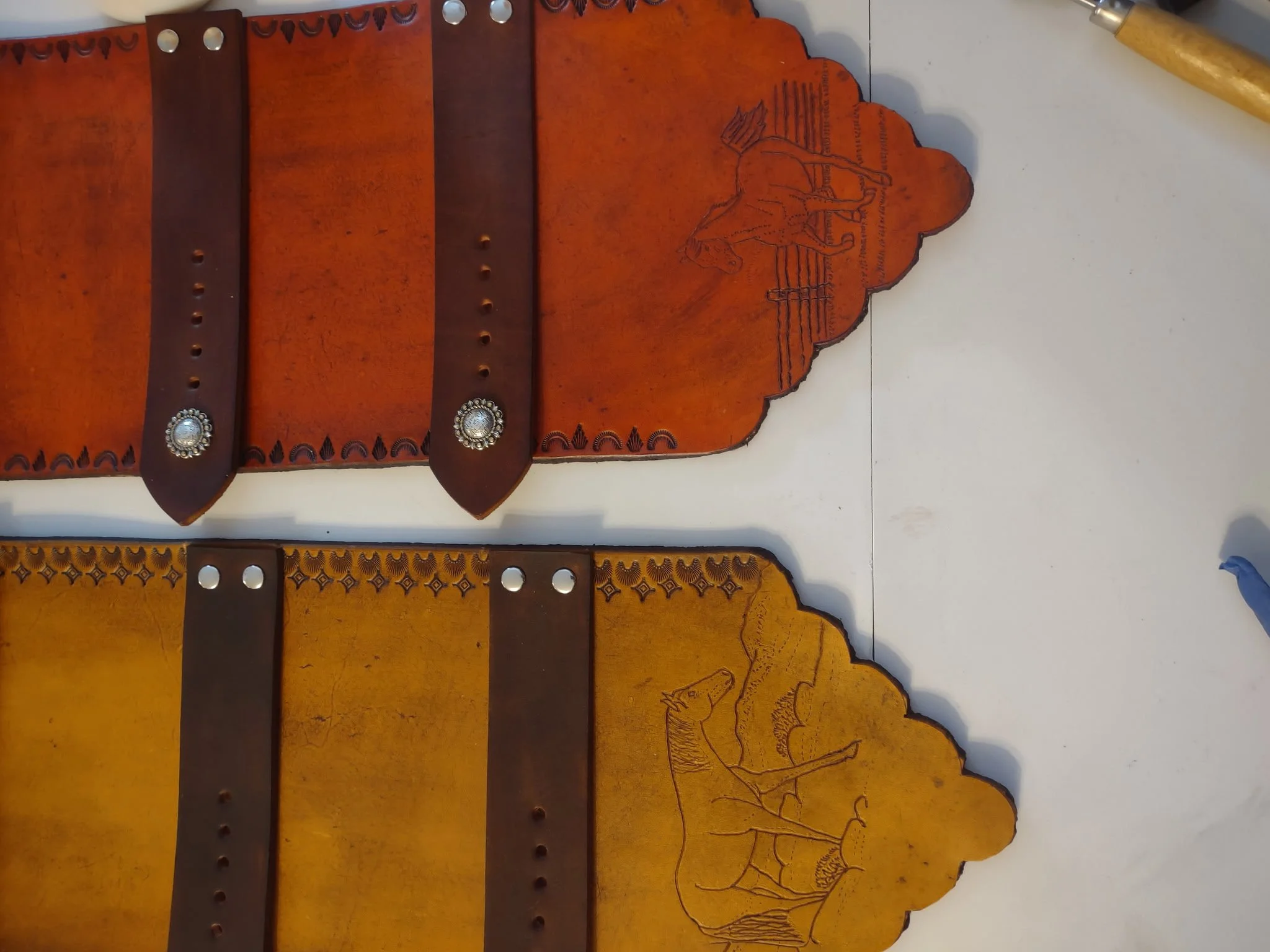 Decorative custom leather belt buckle holders with engraved details, two dark brown horizontal leather straps with silver embellishments.