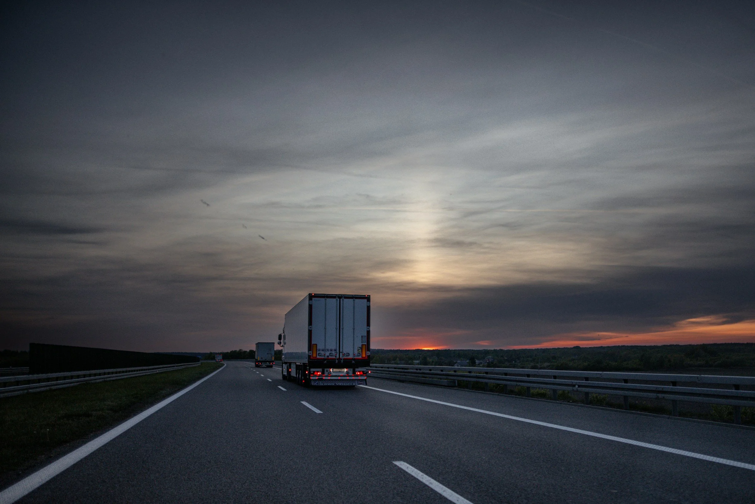 A highway with multiple trucks driving during sunset or sunrise, cloudy sky, and a distant horizon.