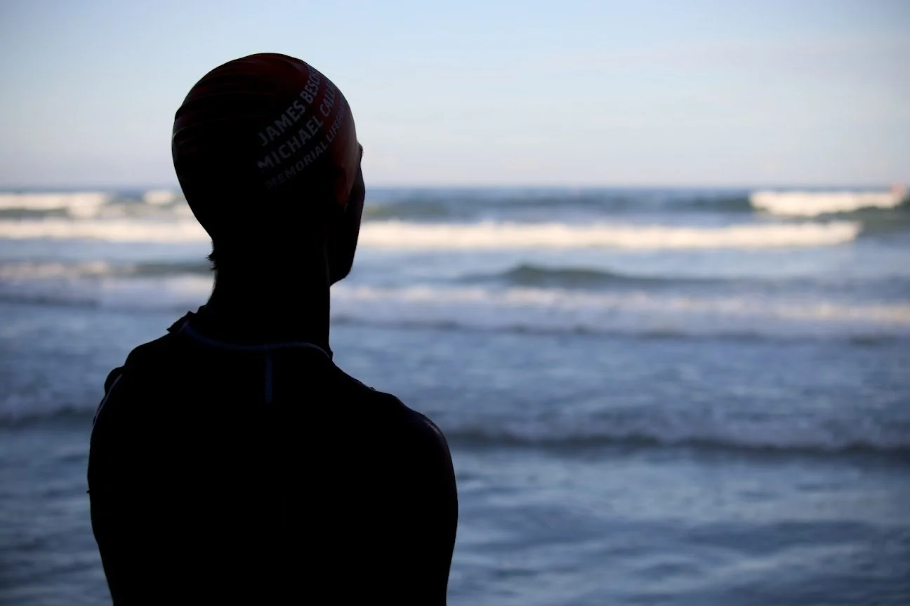 Person wearing a swim cap and face mask, looking at the ocean.