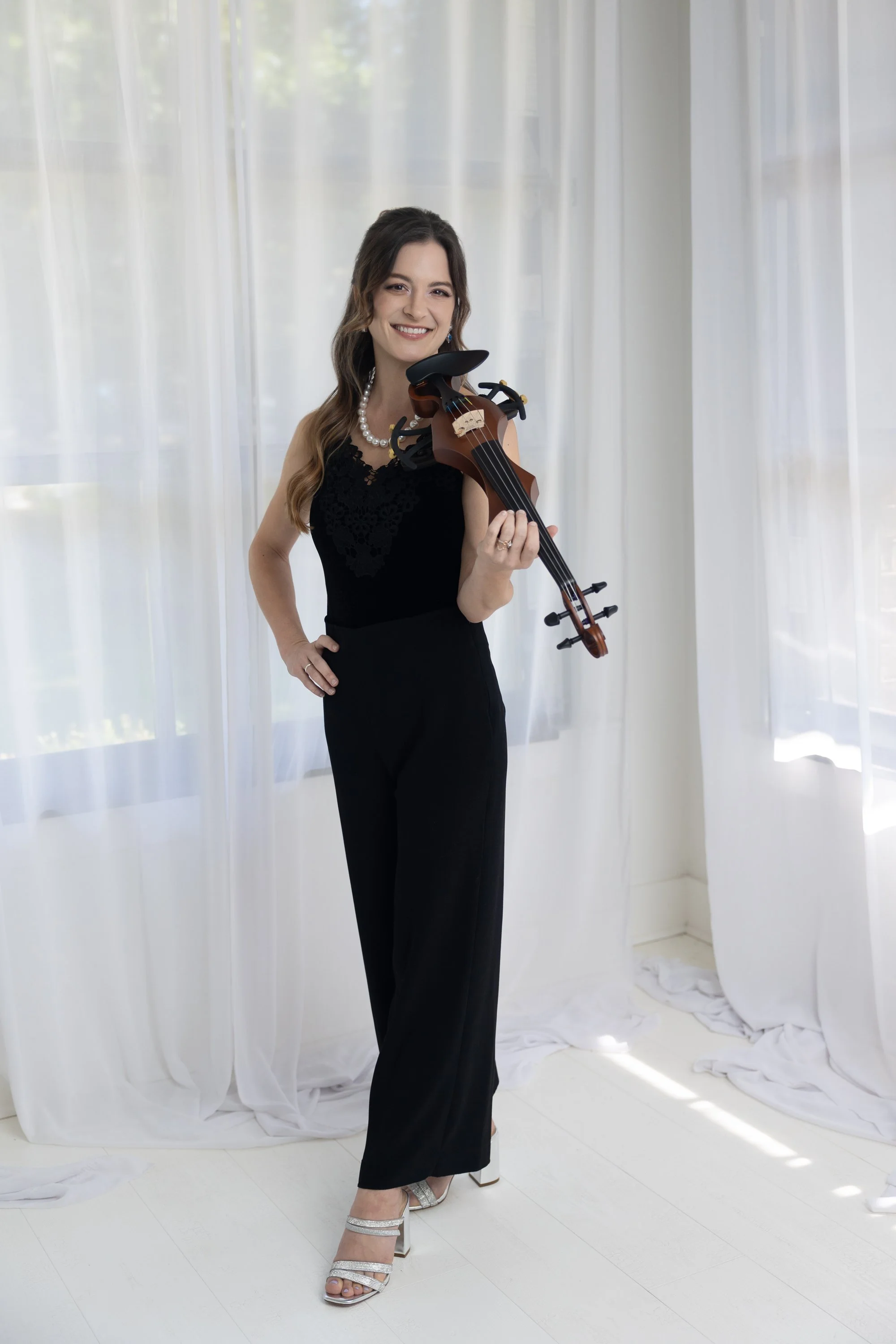 A woman on stage playing the violin with a microphone, eyes closed, under warm lighting with a wooden background.