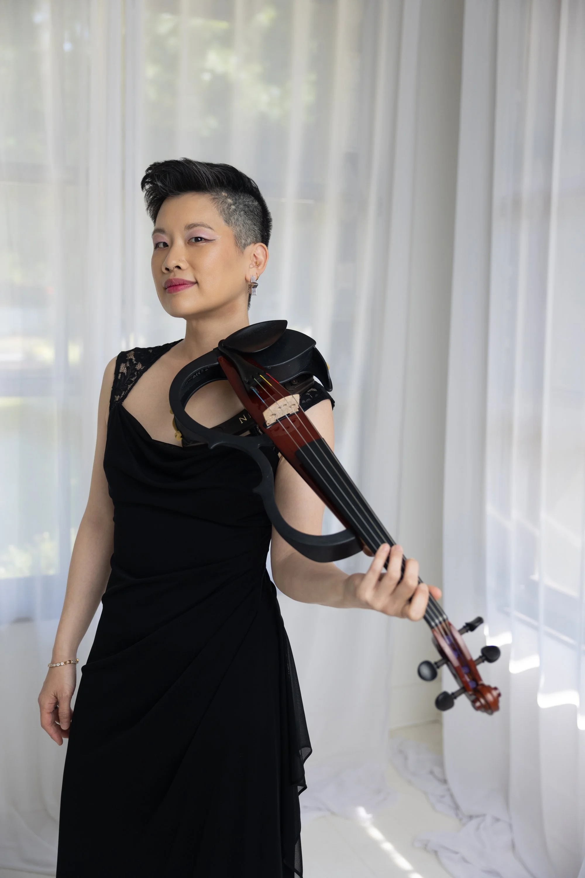 A woman playing the violin outdoors near power lines and trees at dusk or dawn with a greenish sky.