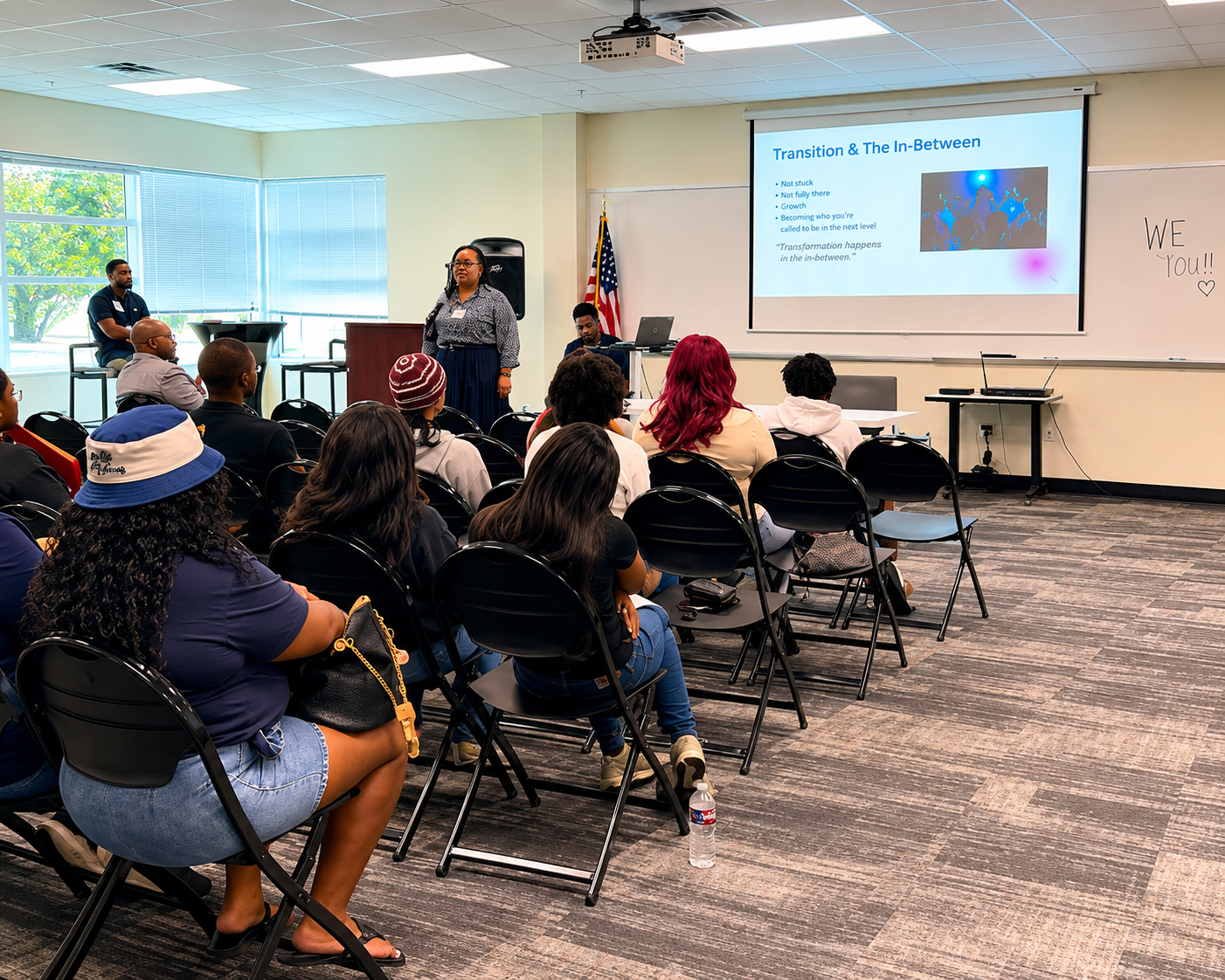 The Keynote Speaker, Dr. Renatta Lindsey, stands near a screen displaying a slide titled 'Transition & The In-Between' - Speaking to the students about, "The Power of One Decision" 