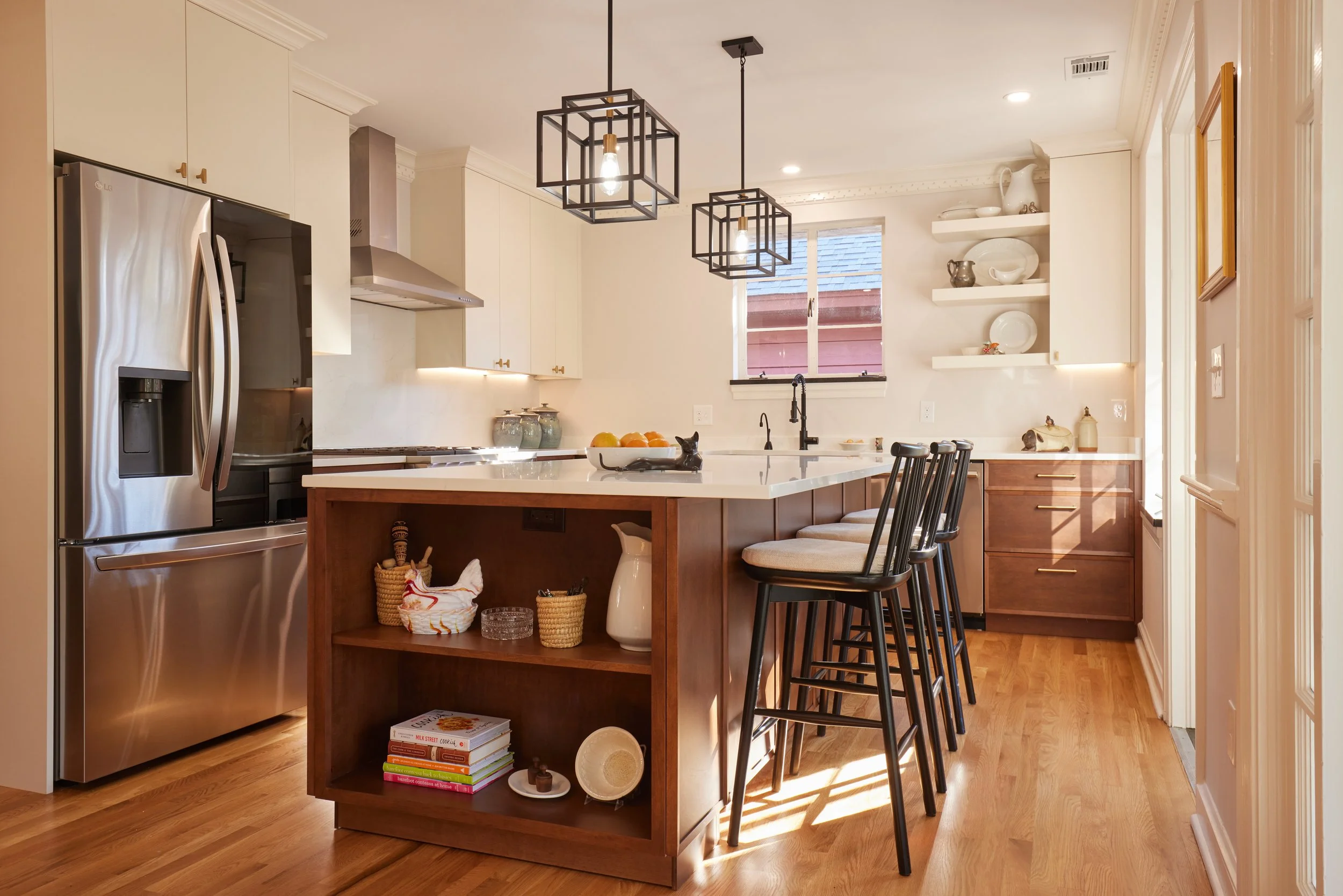 Modern kitchen with white cabinets, wooden island, black chairs, stainless steel refrigerator, and open shelves with dishes, sunlight streaming in.