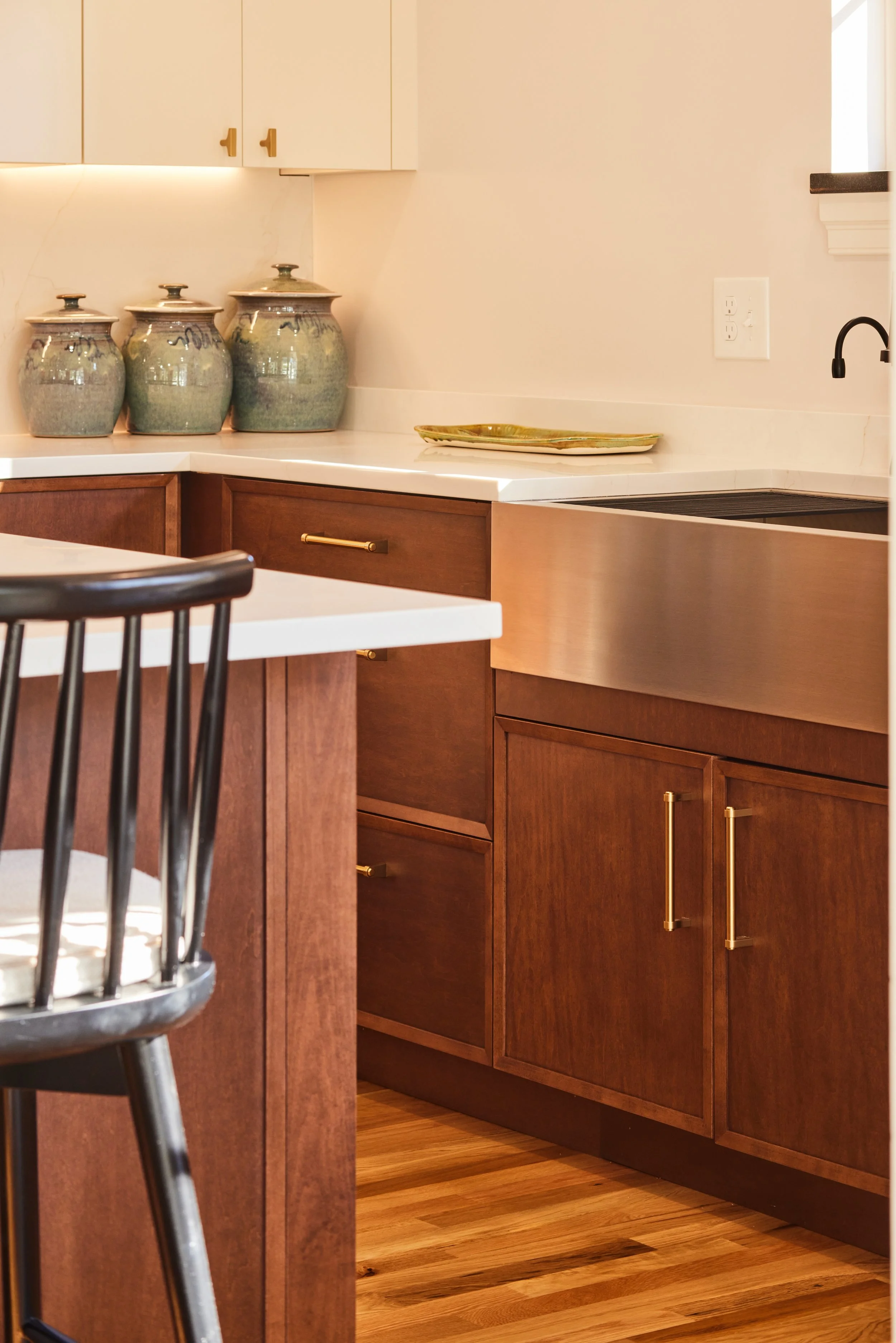 Close-up of a kitchen counter with three decorative ceramic jars, a yellowish-green plate, and wooden cabinets with gold handles.