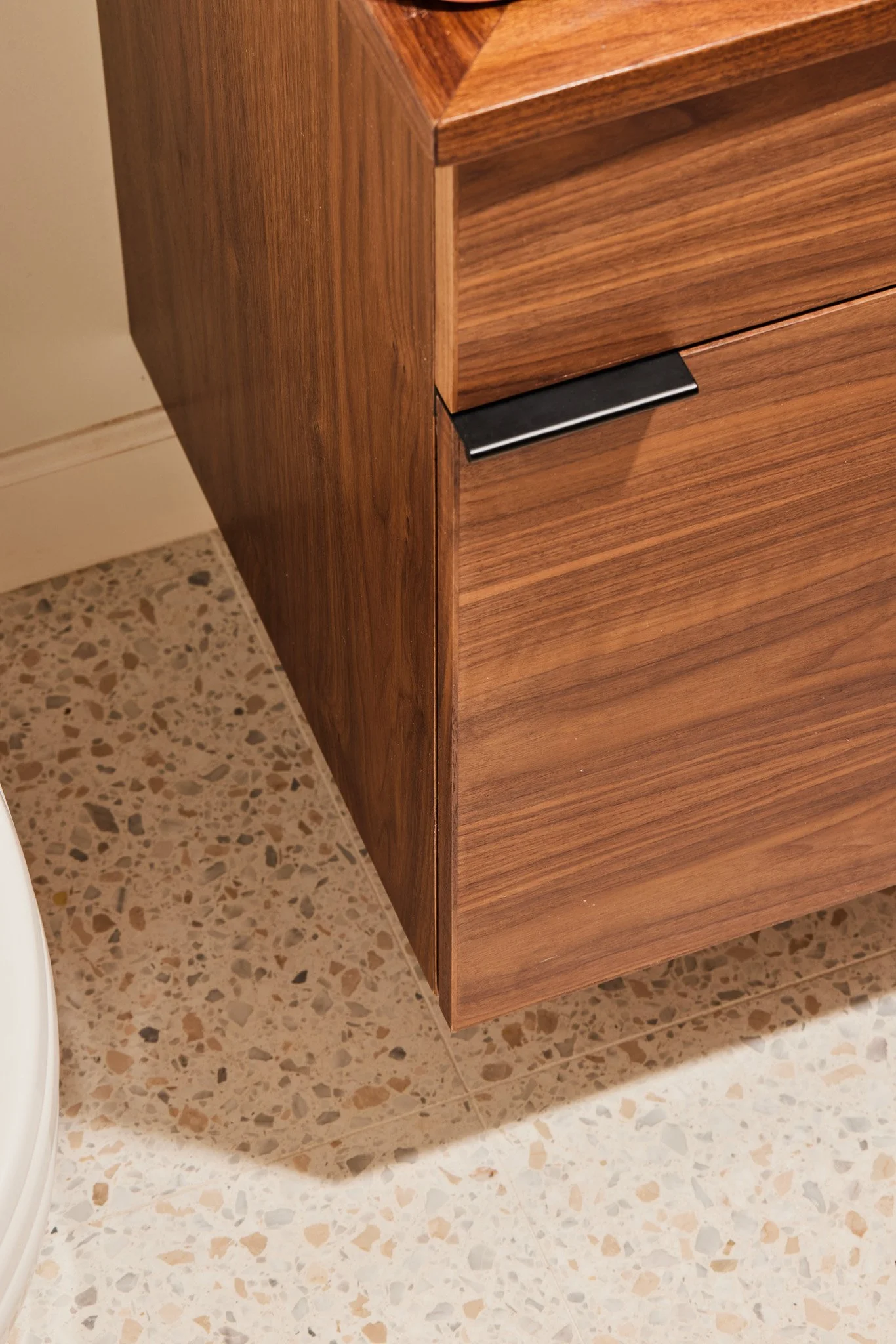 Close-up of a wooden cabinet with a black handle, on a terrazzo floor.