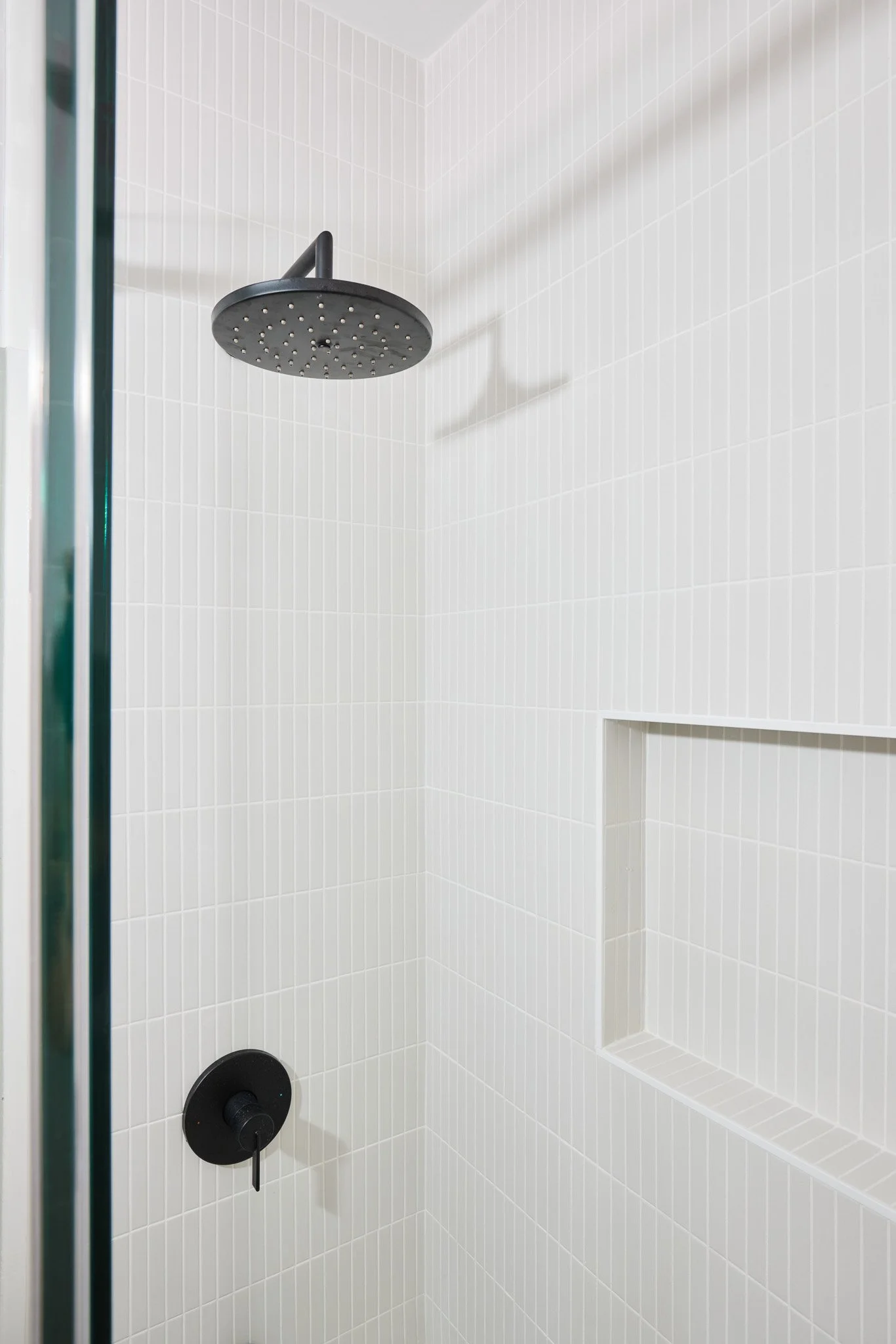 Empty shower with black rain showerhead, black control knob, and built-in wall niche, with white tiled walls.