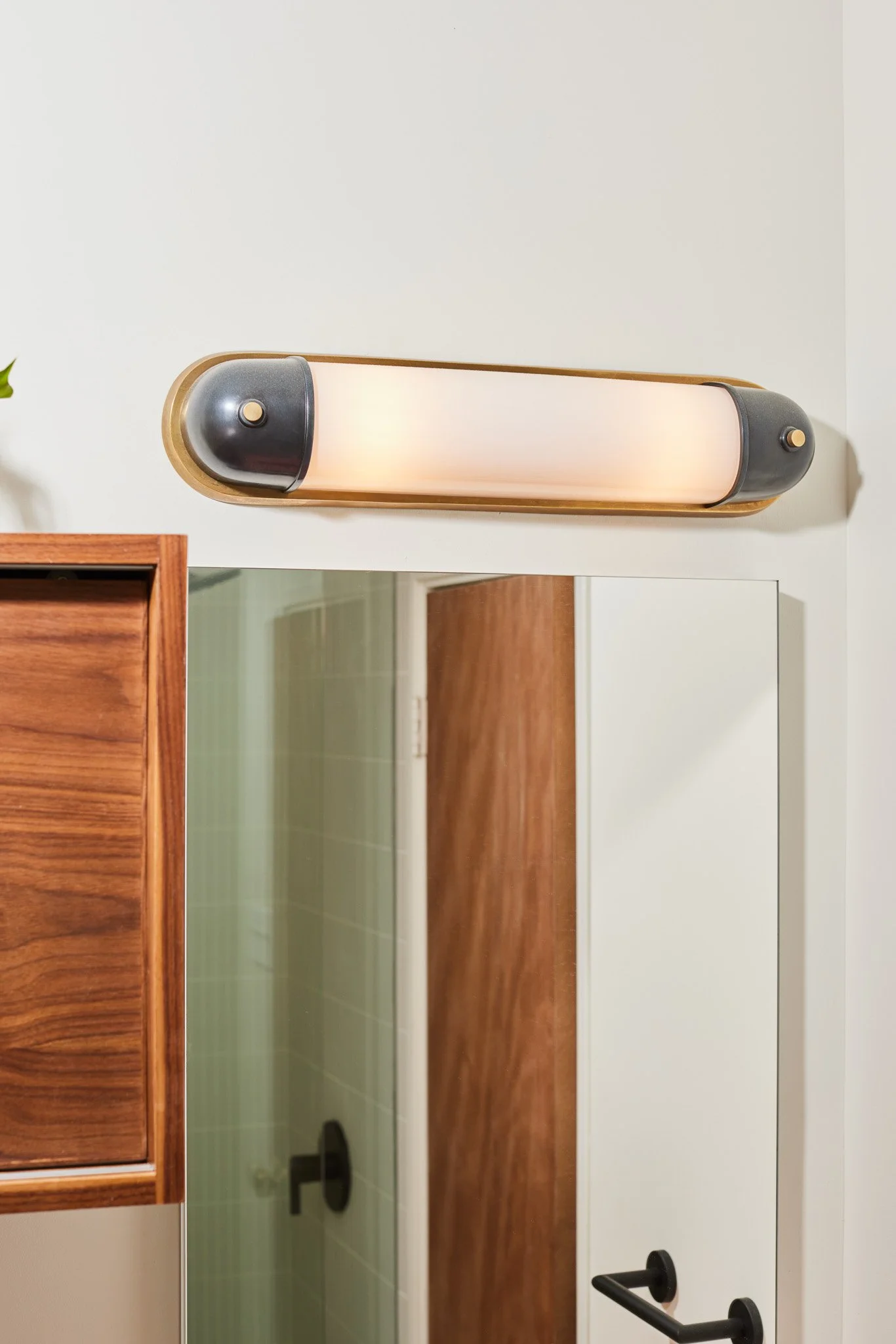 Modern wall-mounted light fixture with a rounded wooden frame and black accents, installed above a mirror in a bathroom or bedroom.