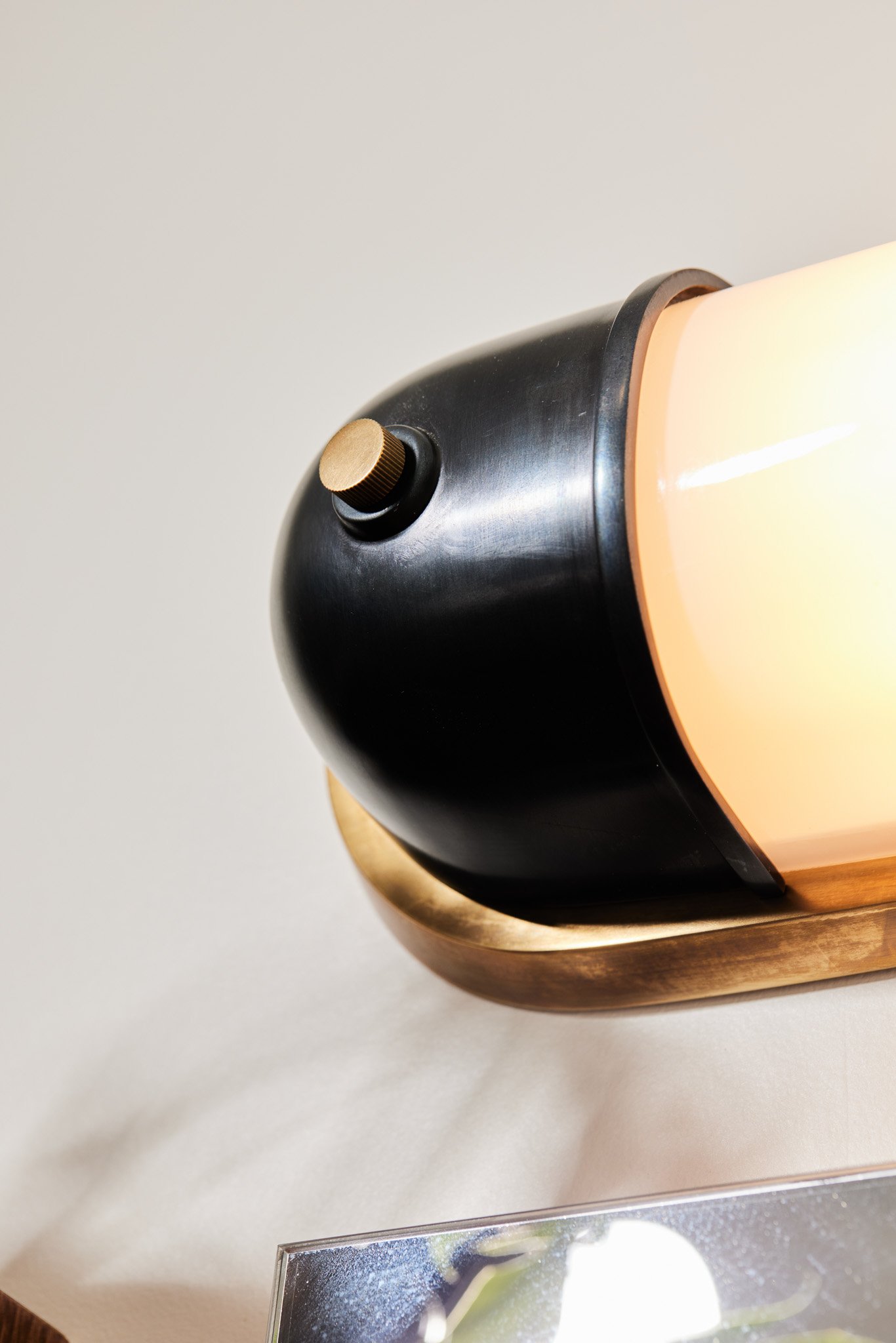 Close-up of a modern wall-mounted lamp with a black and gold color scheme, featuring a rounded black body, a gold knob, and a warm light bulb emitting a soft glow.
