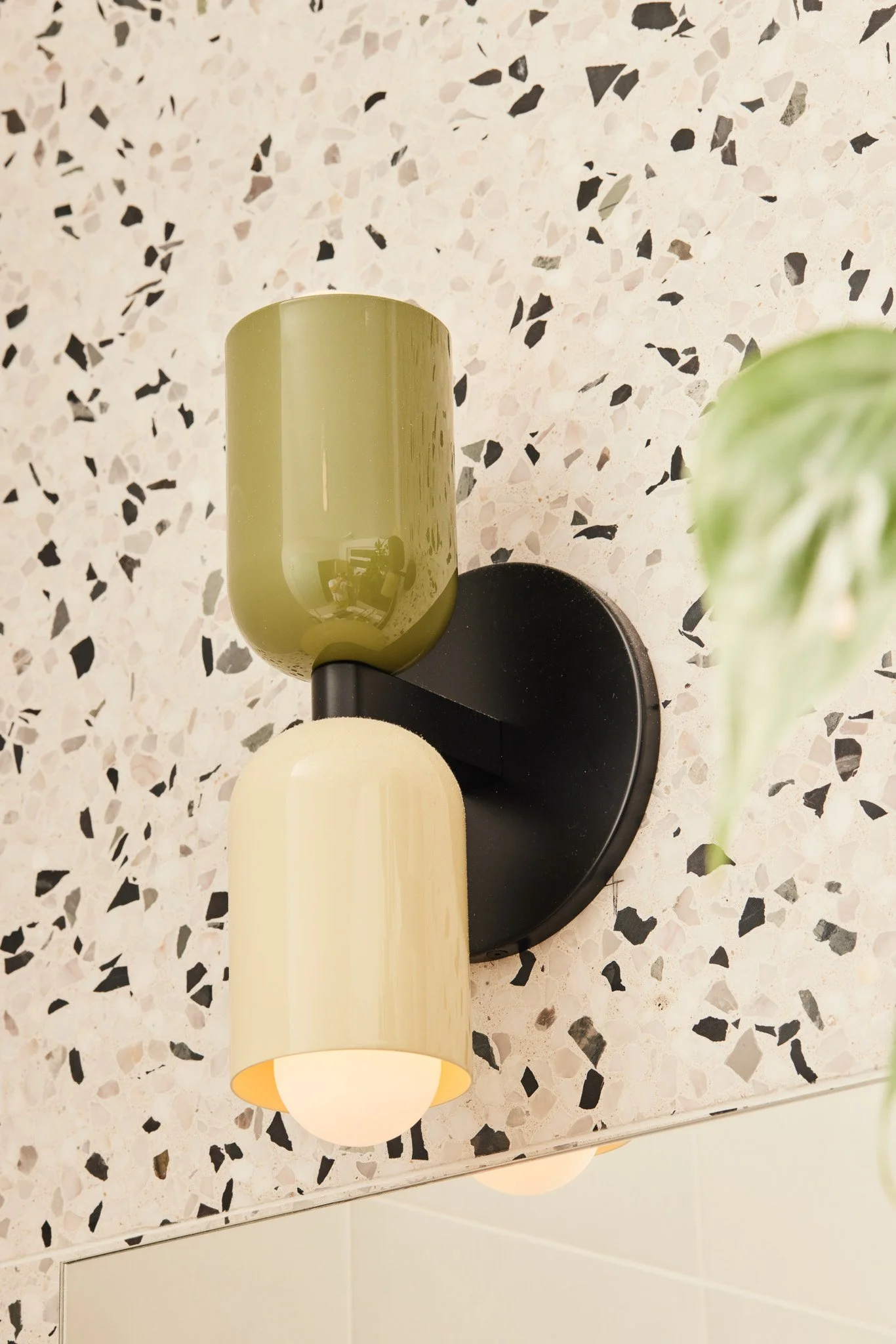 Close-up of two modern wall-mounted lamps, one green and one beige, on a terrazzo wall in a room.