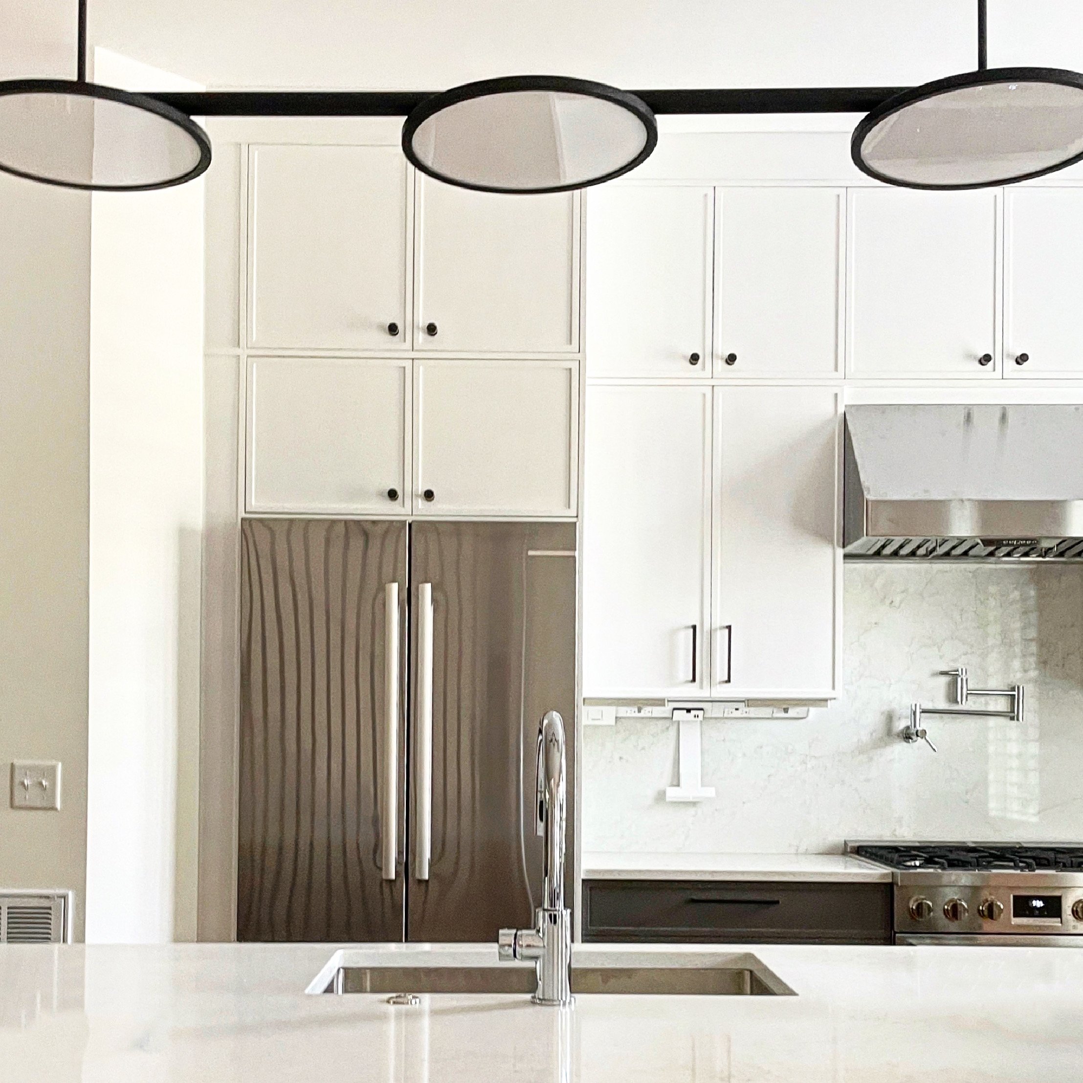 Modern kitchen with white cabinets, stainless steel refrigerator, marble countertops, a sink, and a stove with a range hood.