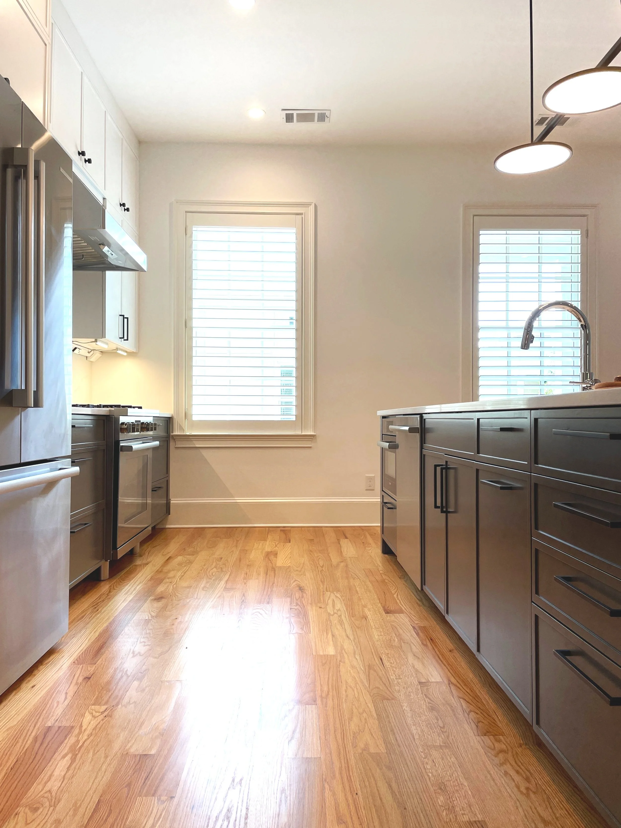Modern kitchen with natural light, wooden floor, white cabinets, and stainless steel appliances.