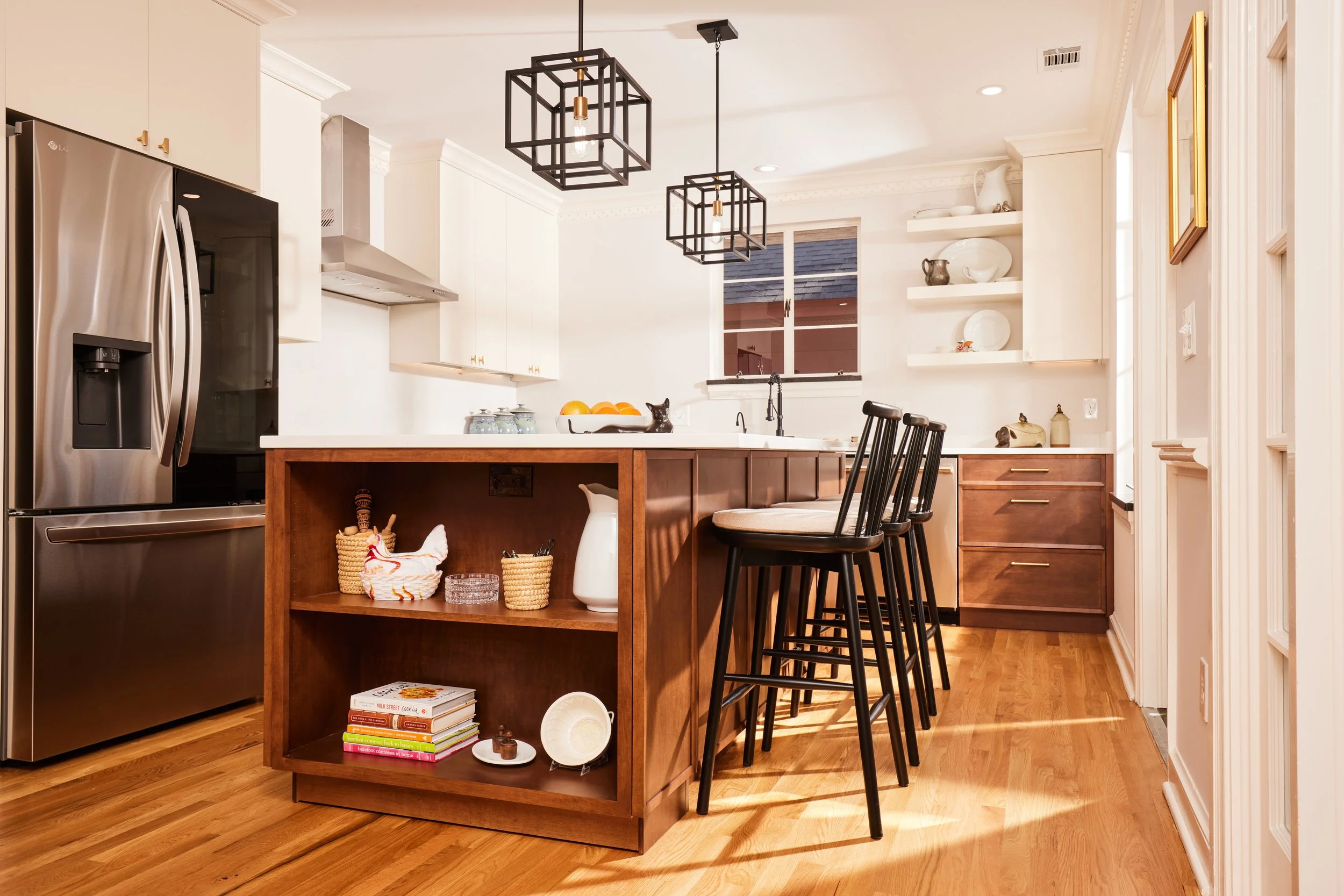 Modern kitchen with white cabinets, wooden island, black bar stools, stainless steel refrigerator, open shelves with dishes, and pendant lighting.