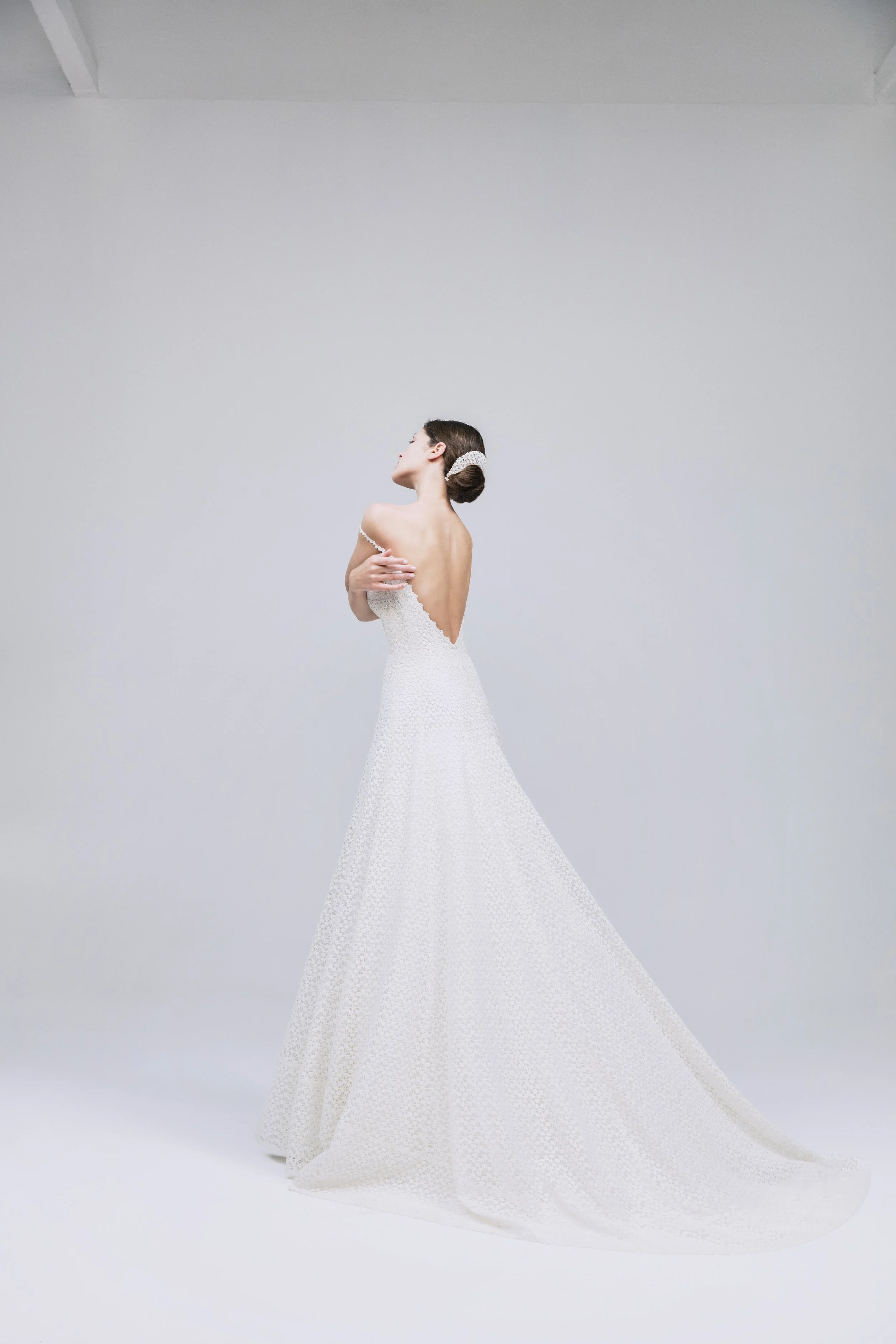 Donna in abito da sposa bianco con acconciatura raccolta, che posa davanti a uno sfondo bianco monotono, in modo artistico.