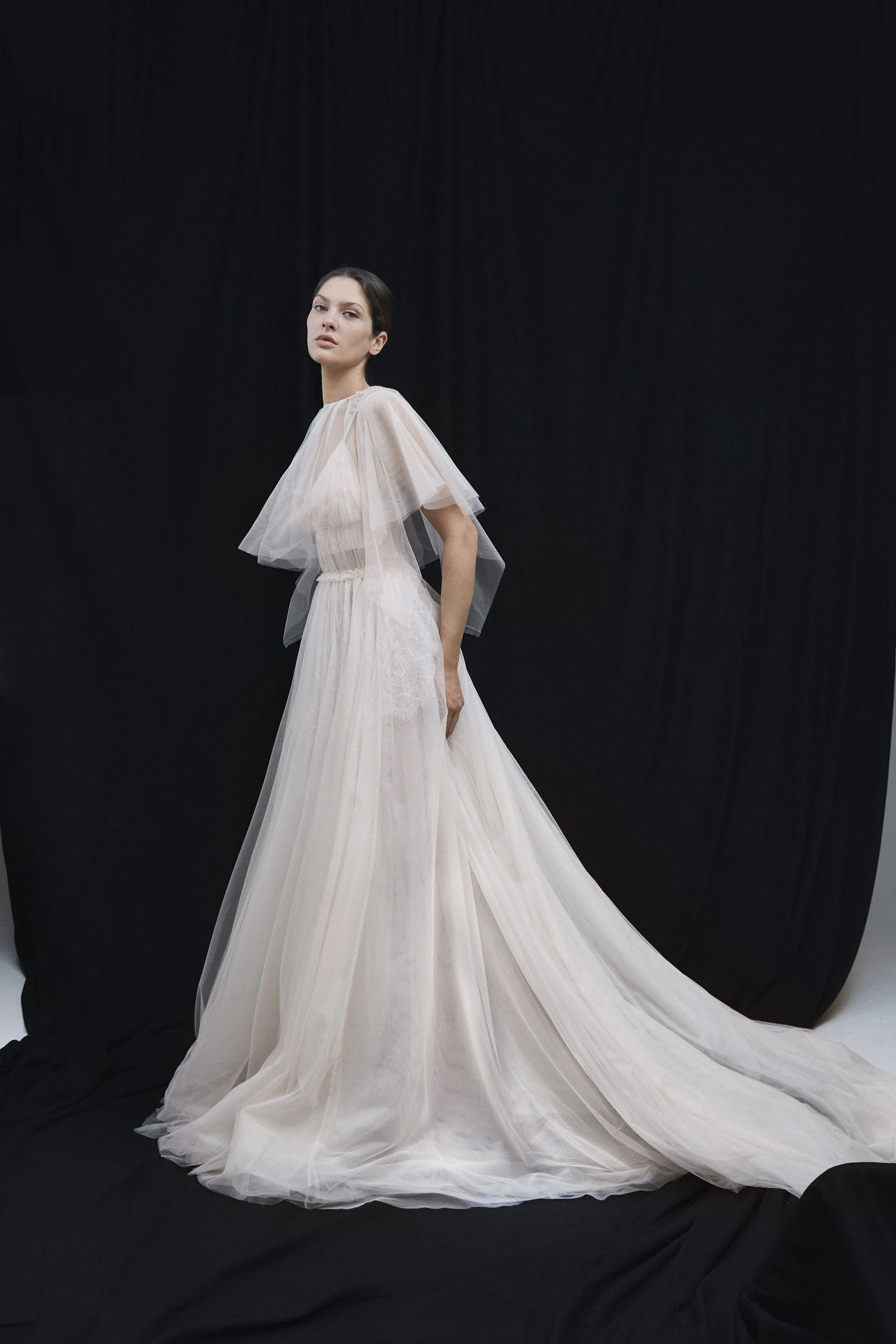 Modella in abito da sposa bianco con gonna lunga in tulle, sfondo nero.