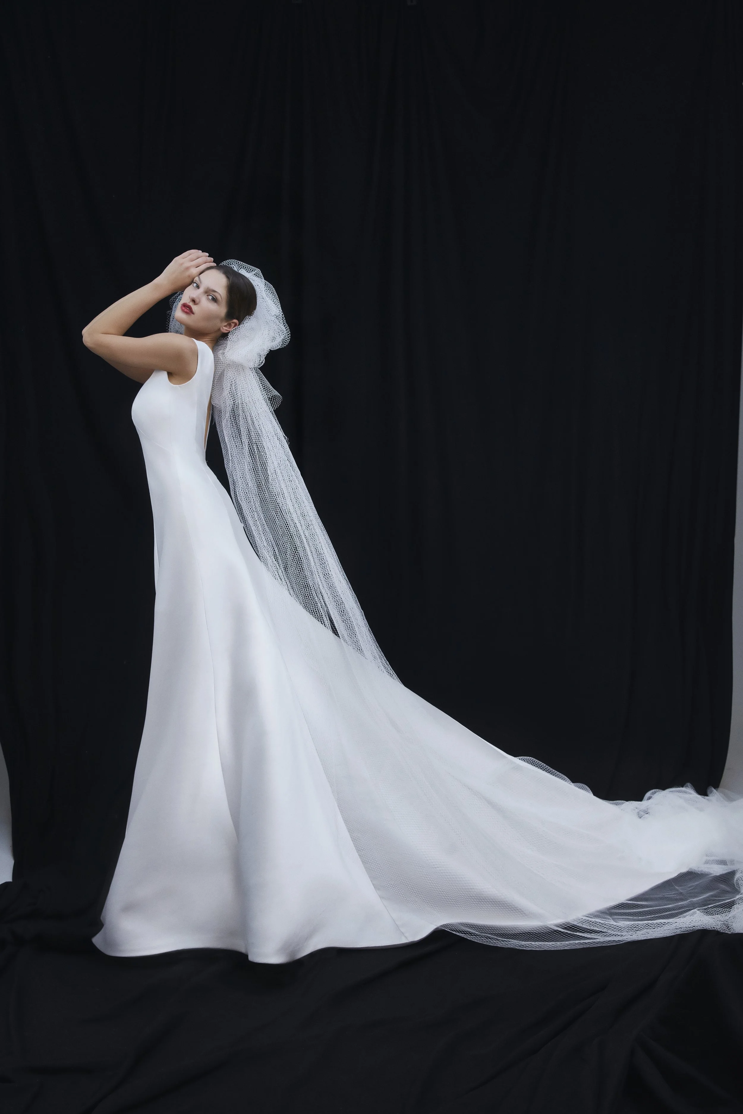 Una donna in abito da sposa bianco con velo, posa davanti a uno sfondo nero.