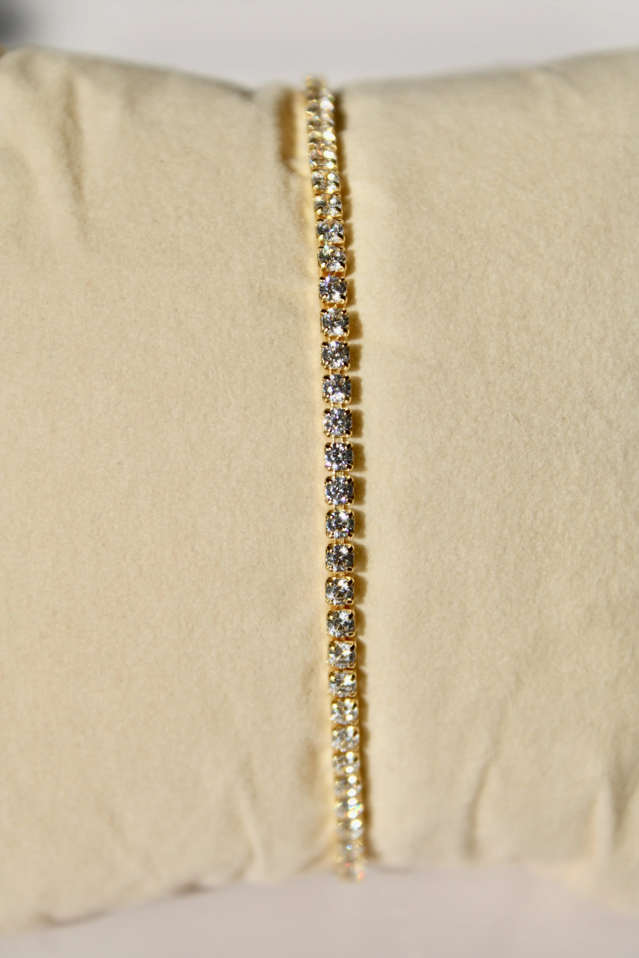 Close-up of a gold chain necklace with small diamonds, displayed on a beige jewelry holder.