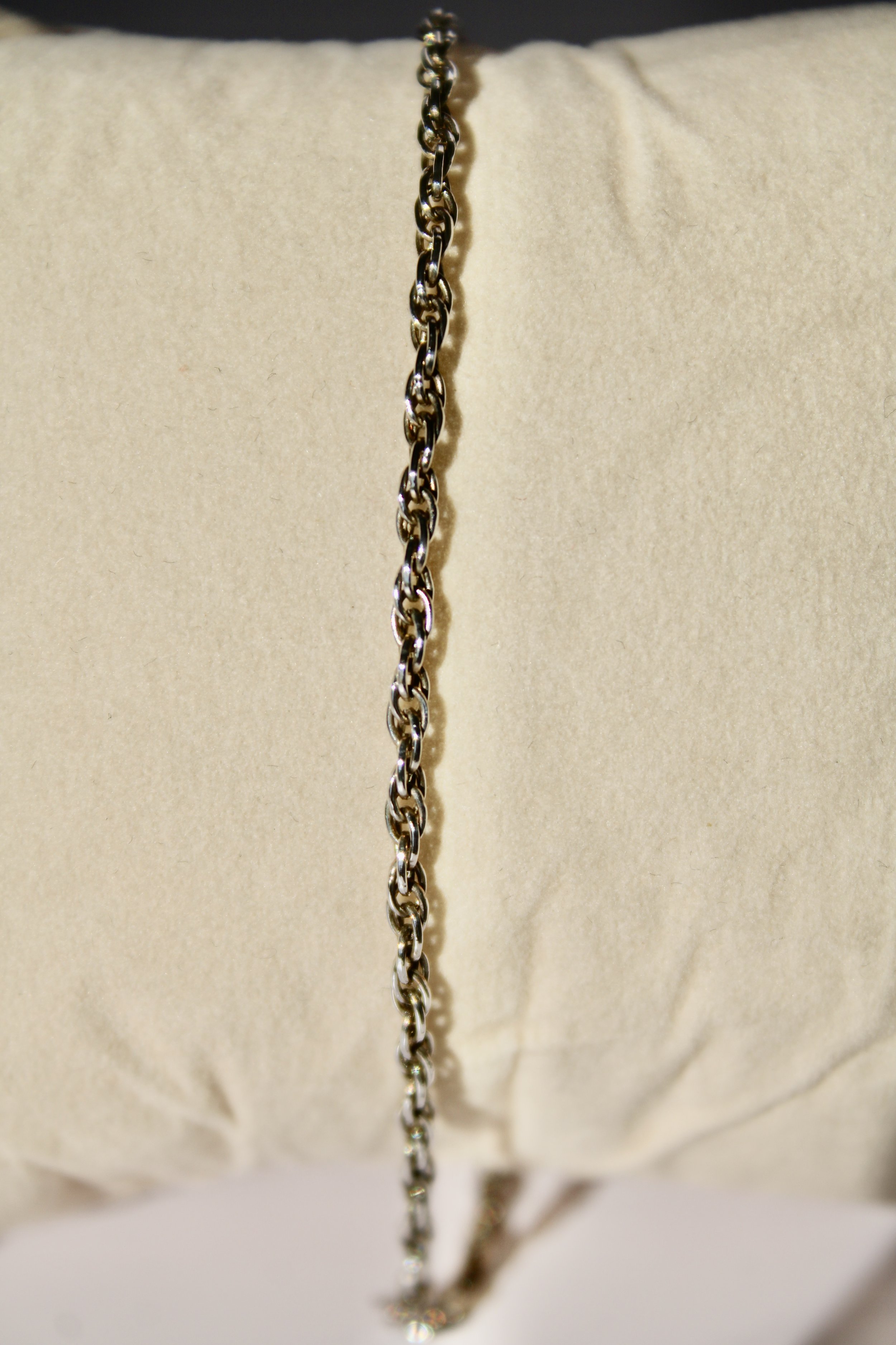 Close-up of a silver chain necklace hanging against a beige background.