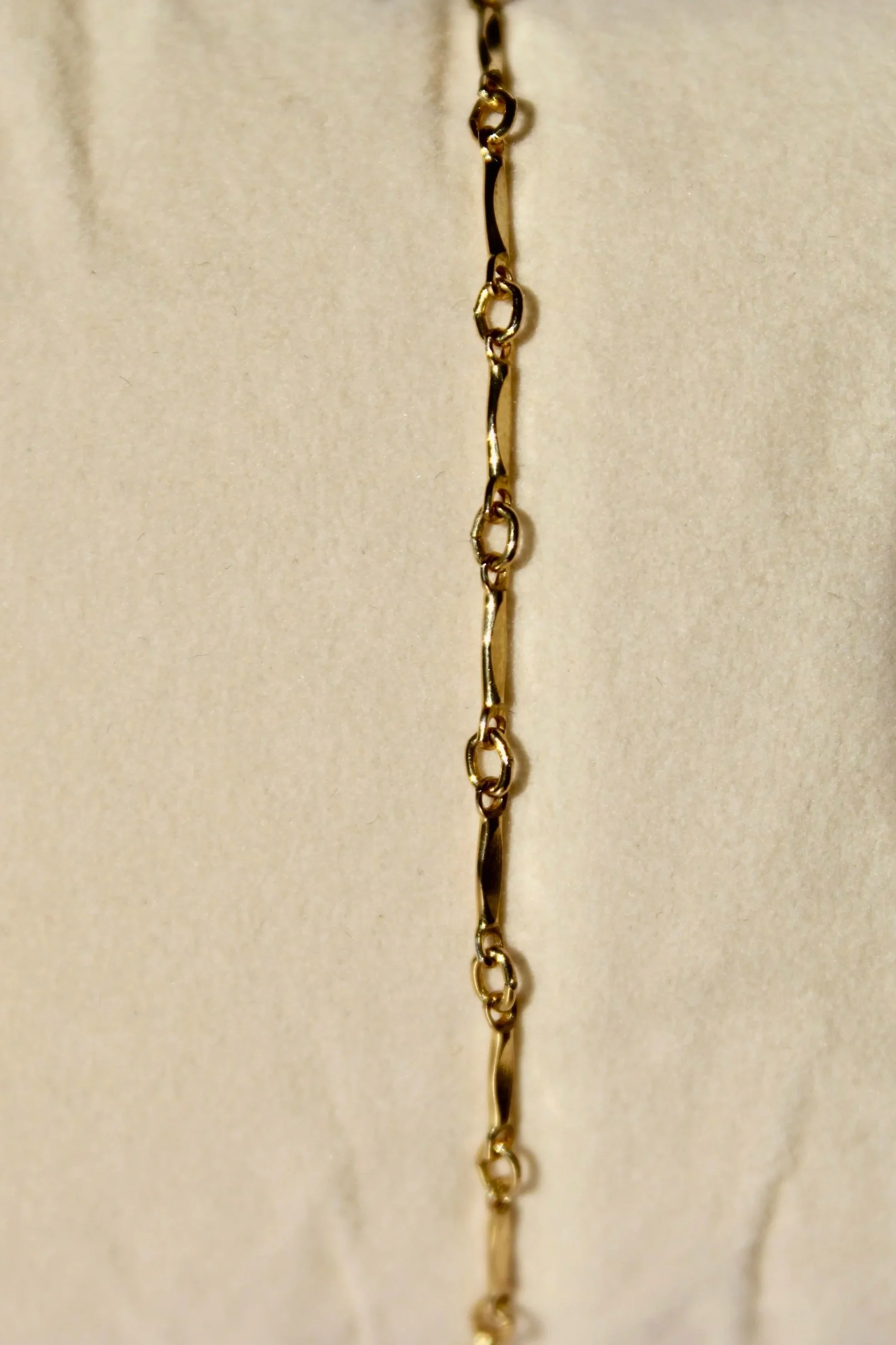 A close-up of a gold chain necklace with oval and twisted links hanging against a light-colored background.
