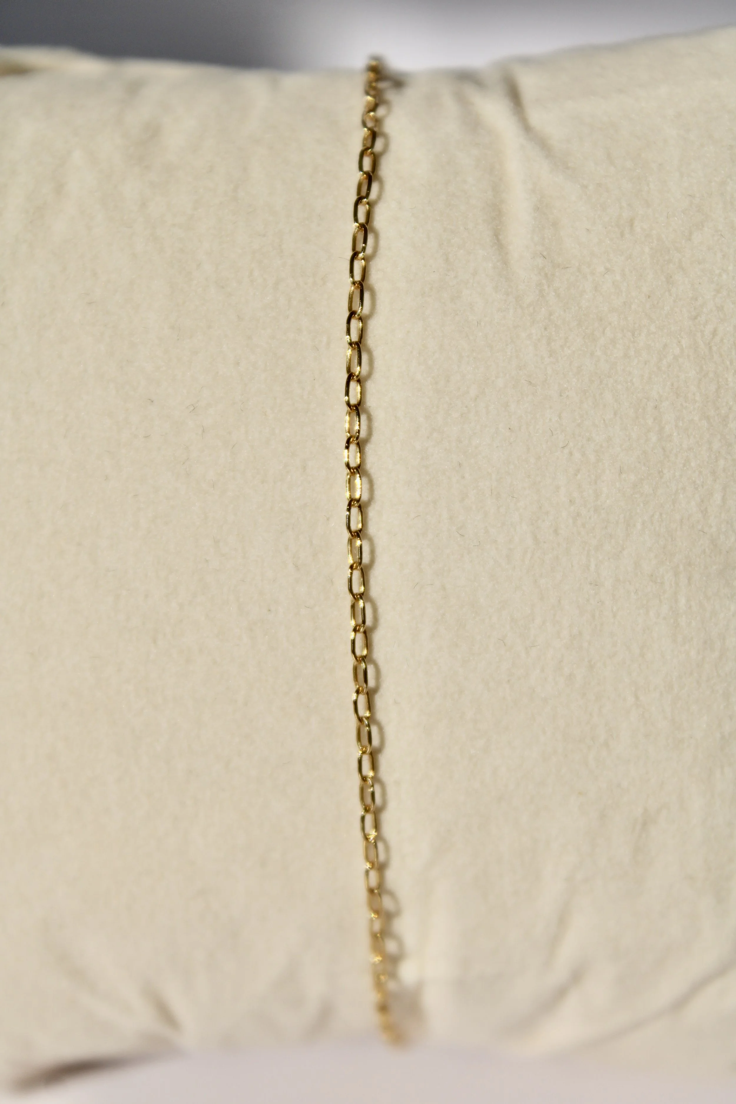 A thin gold chain necklace placed on a beige fabric surface.