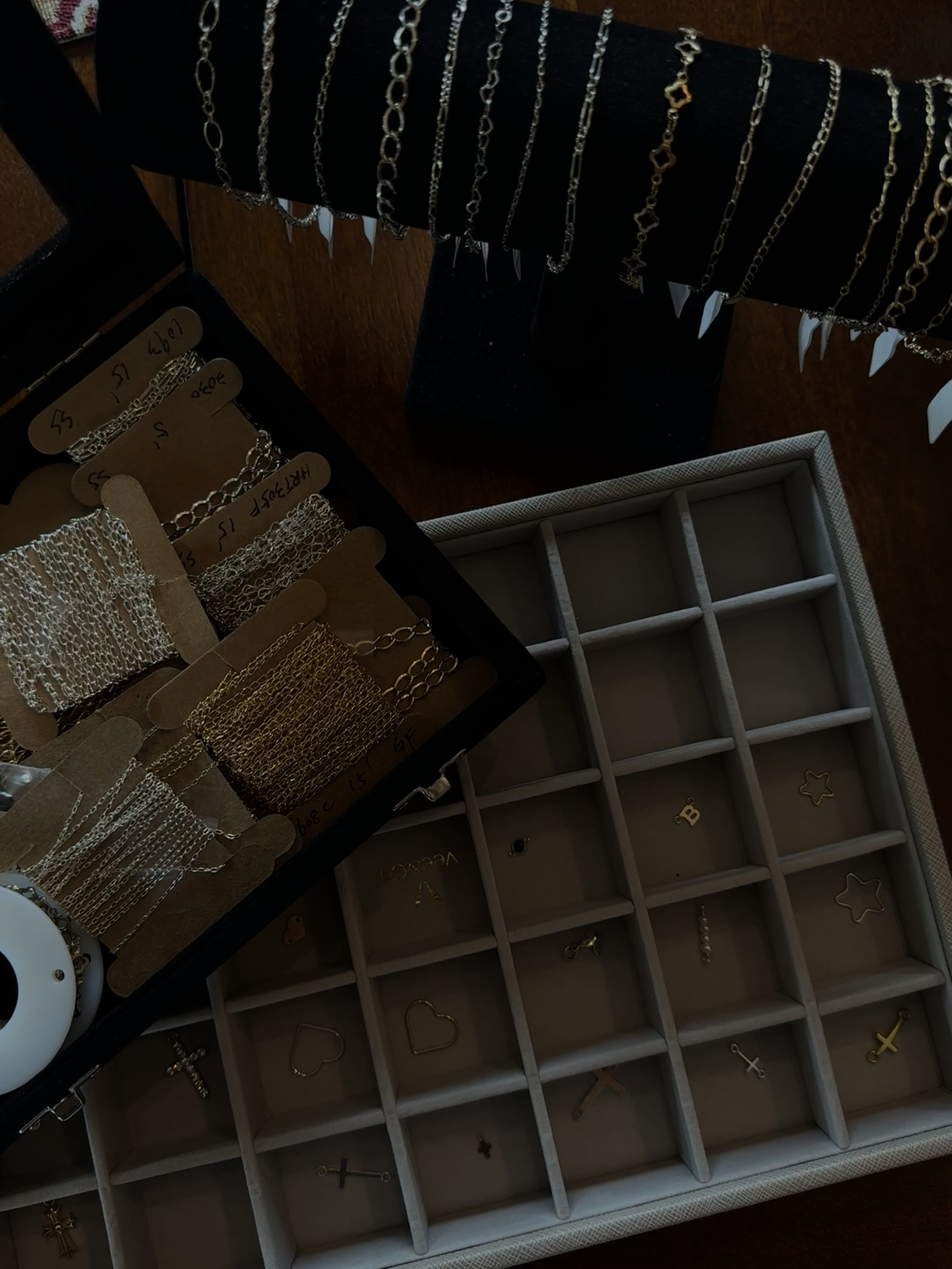 Display of gold and silver jewelry, including chains, bracelets, and charms, arranged on black and cardboard trays, with a white jewelry organizer with compartments and gold star and letter charms.