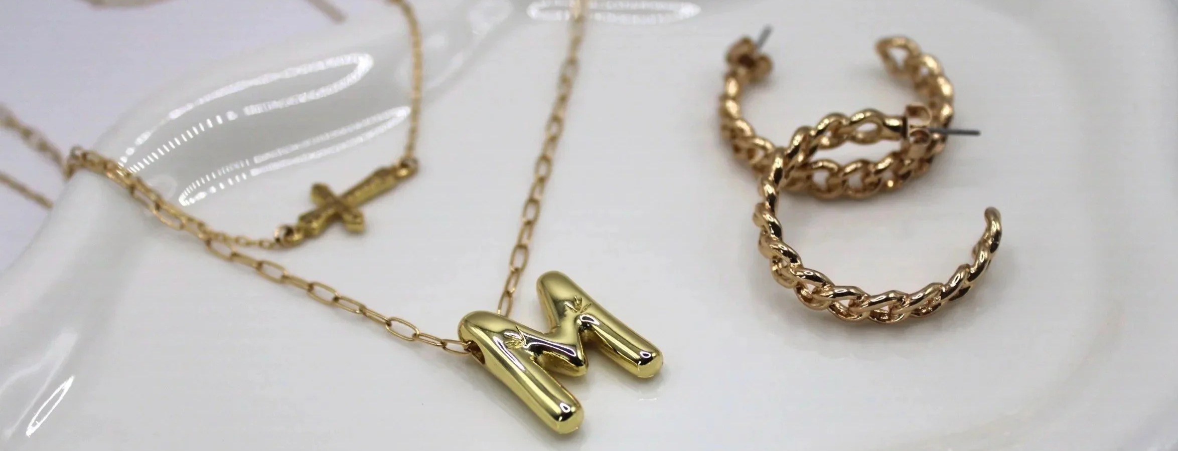 Gold chain necklace with a letter 'M' pendant and gold hoop earrings with a twisted design on a white surface.