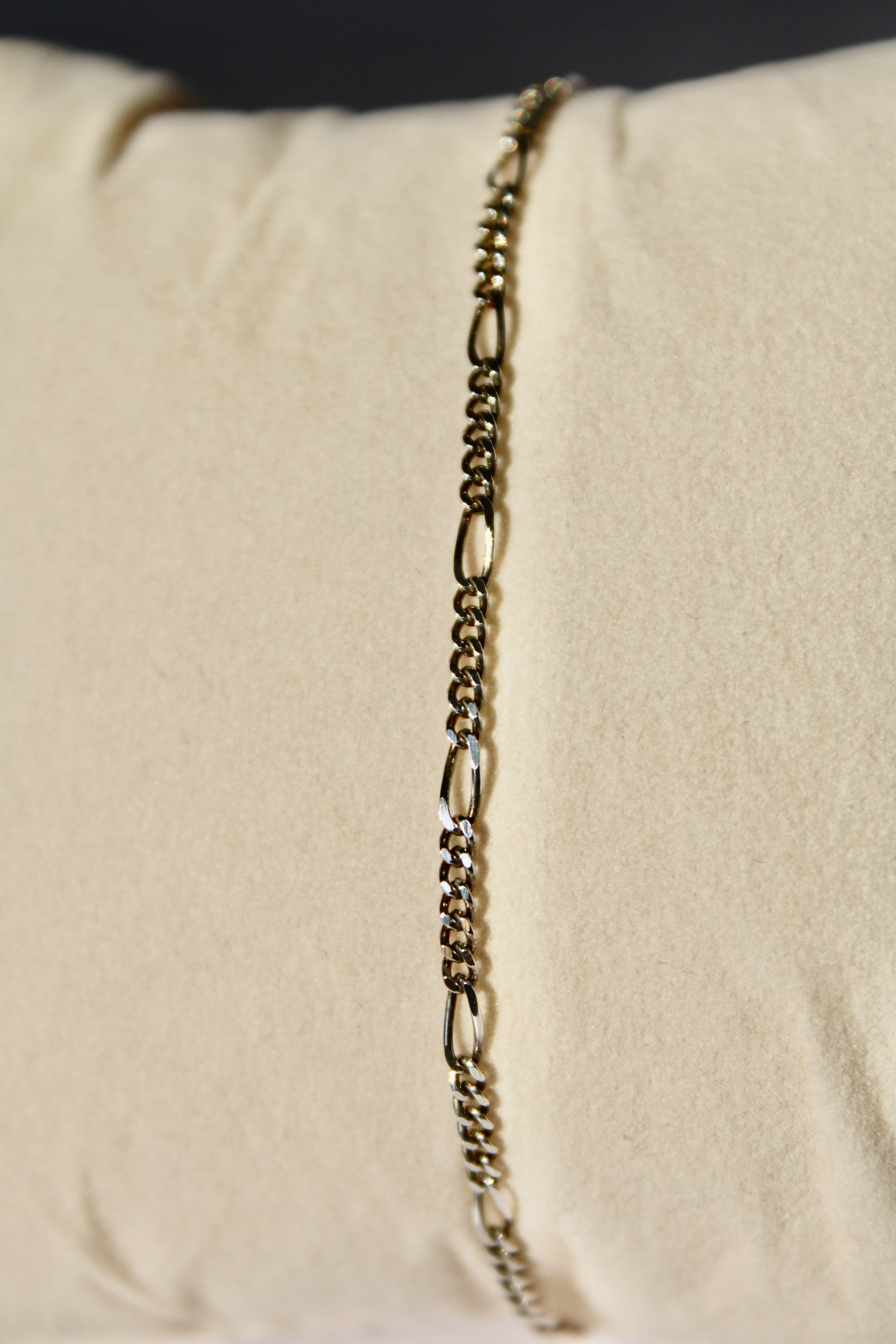 Close-up of a silver chain necklace hanging on a beige padded display.