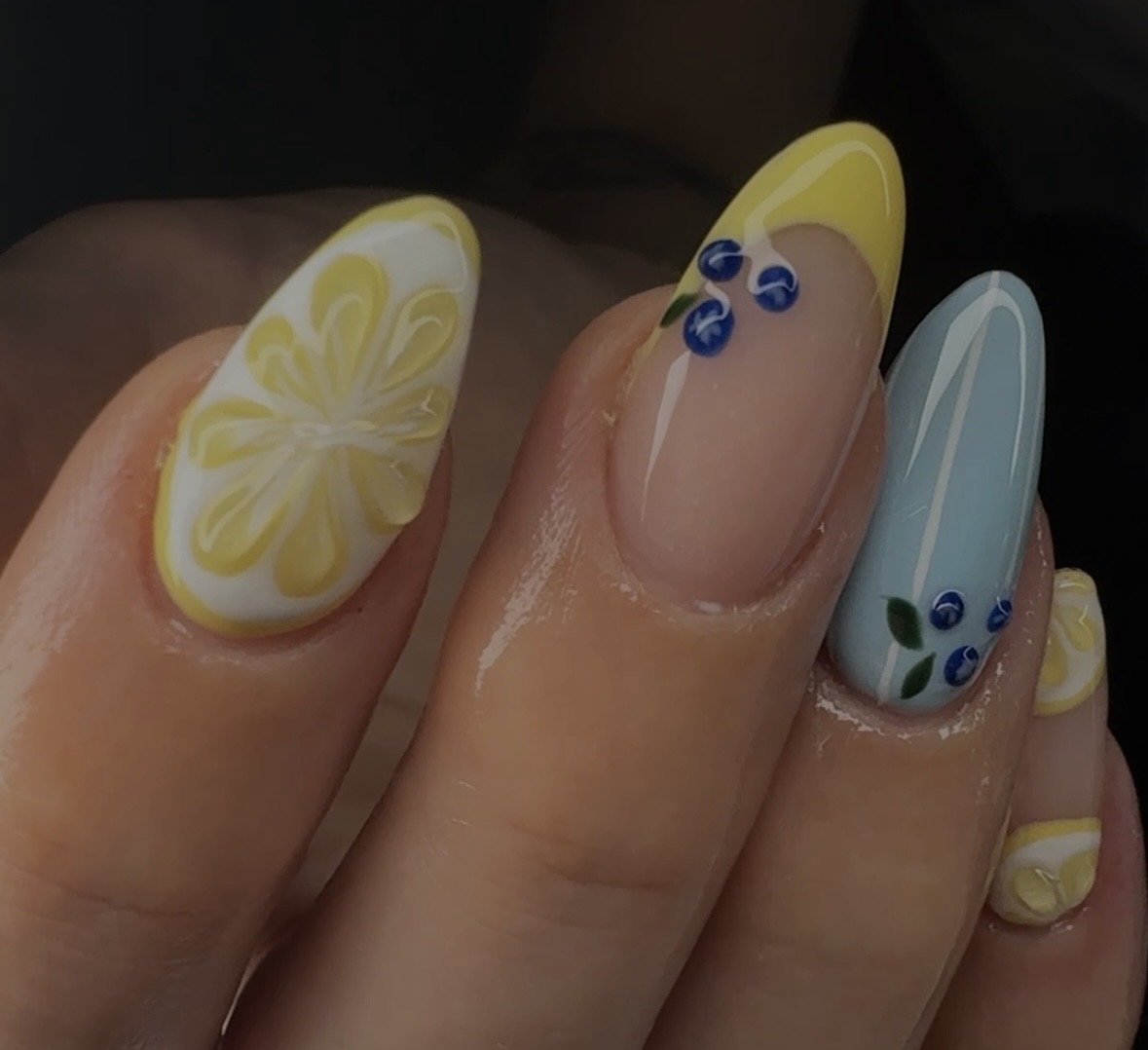 Close-up of manicured nails with lemon, blueberry, and floral nail art designs.