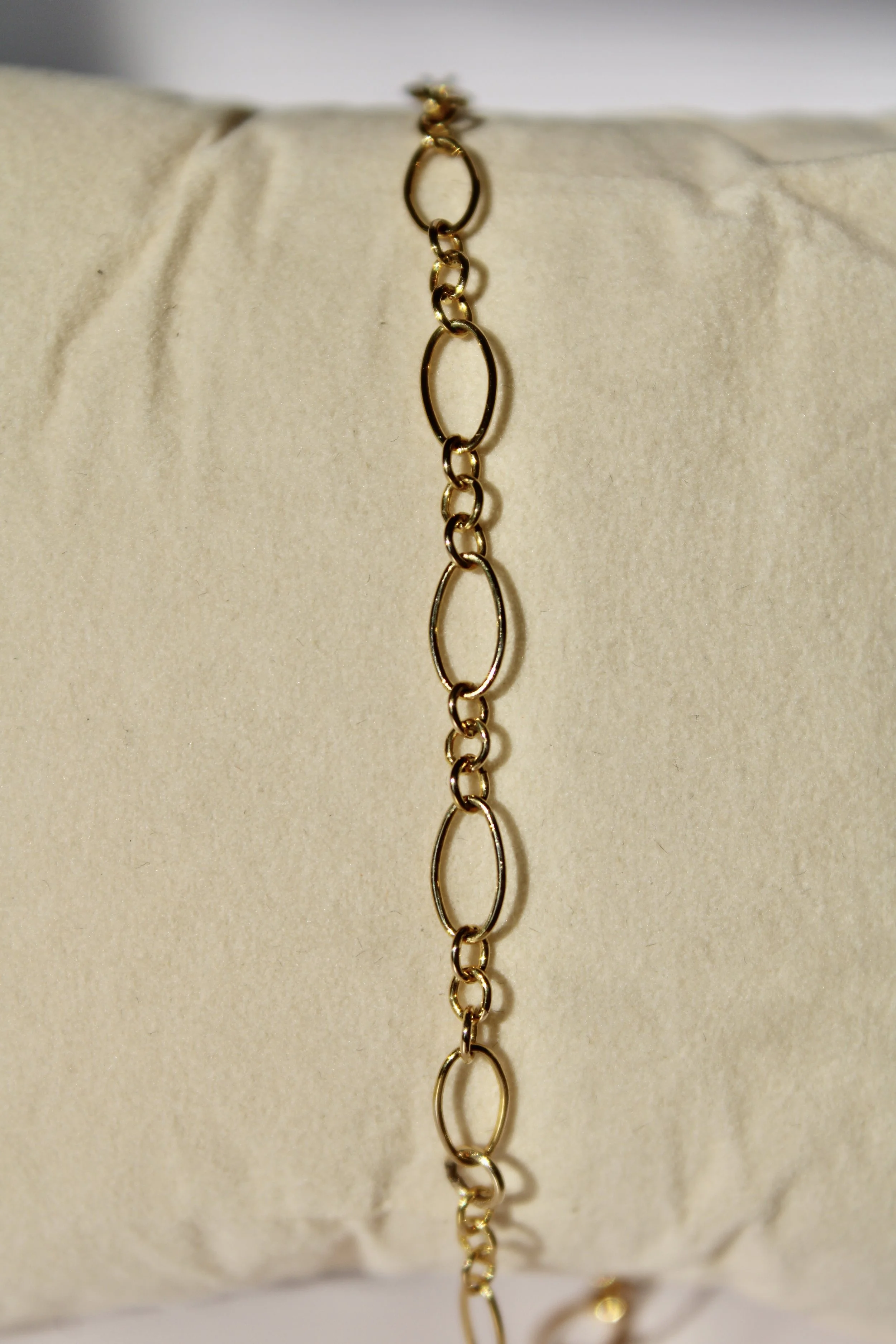 Close-up of a gold chain necklace displayed on a beige cloth or jewelry display stand.