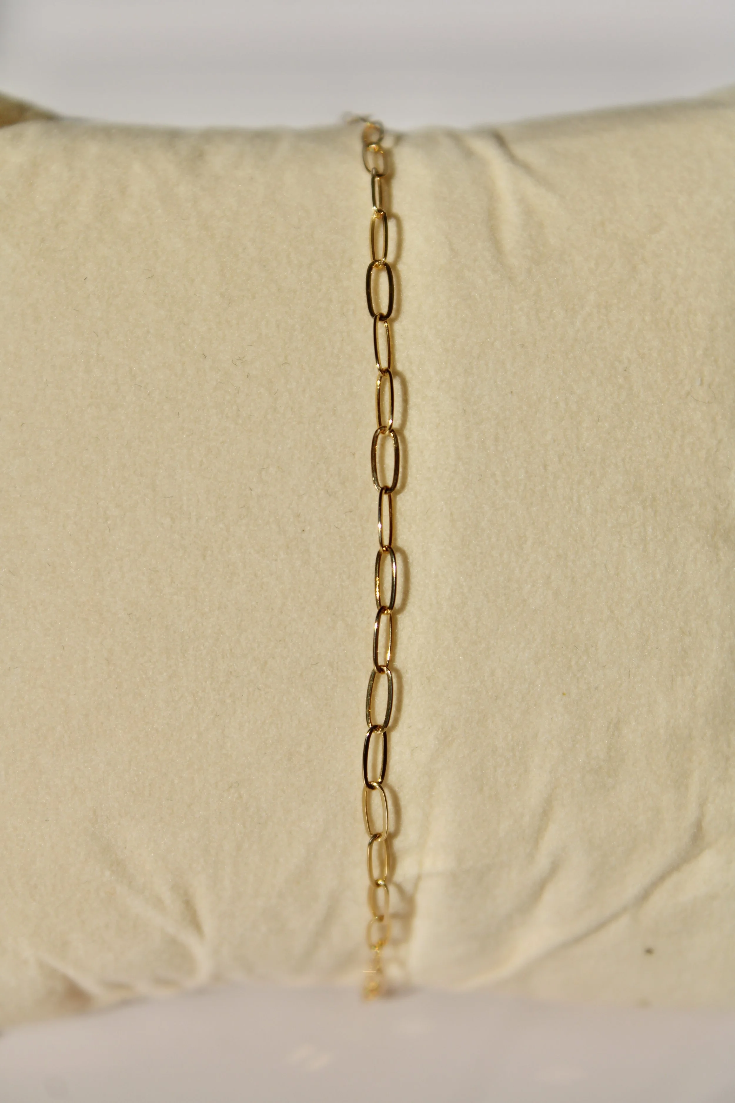 A gold chain necklace draped across a cream-colored fabric pillow.