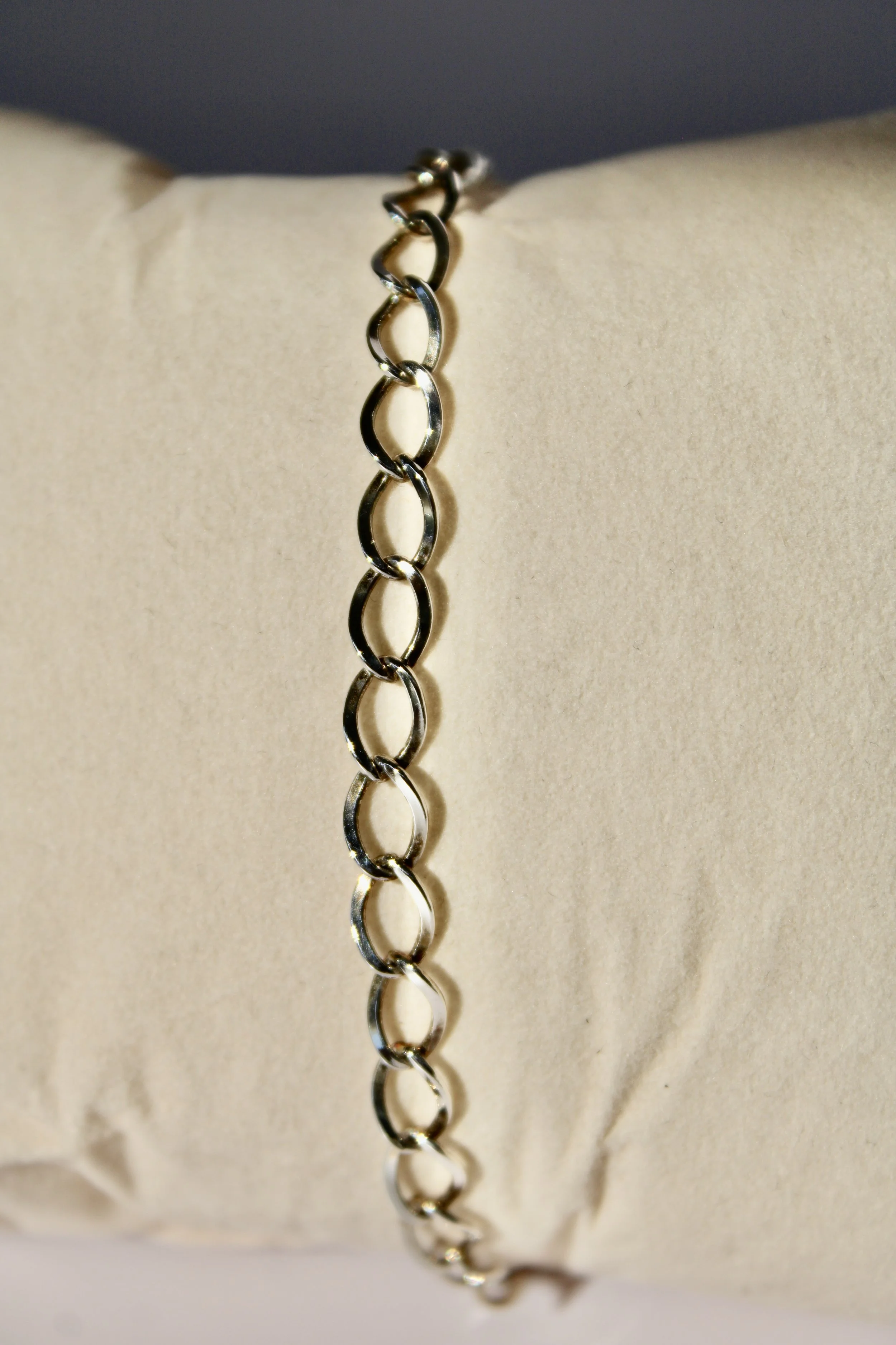 A close-up of a silver chain bracelet resting on a beige cushioned surface.