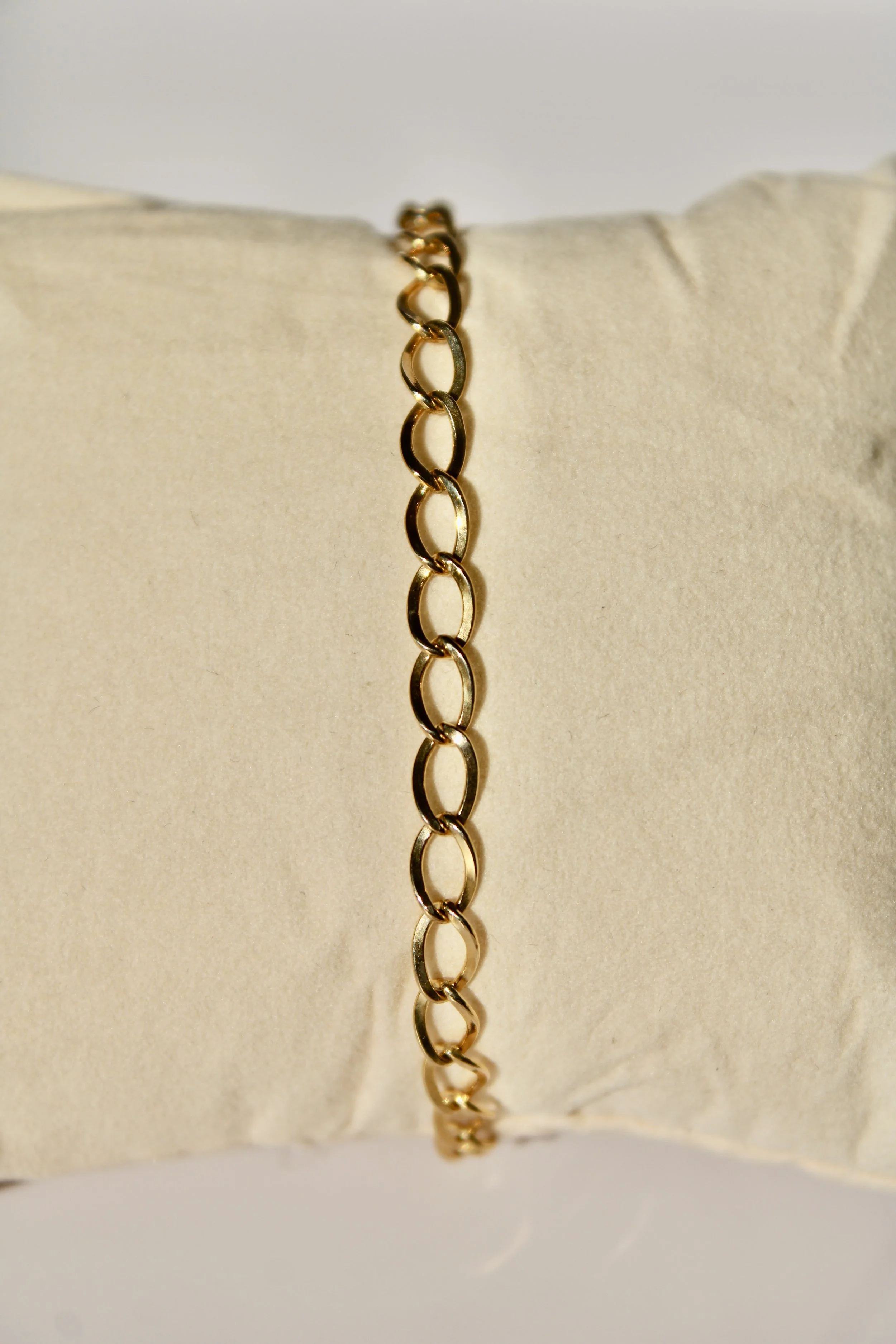 Close-up photo of a gold chain necklace draped over a beige cushion.