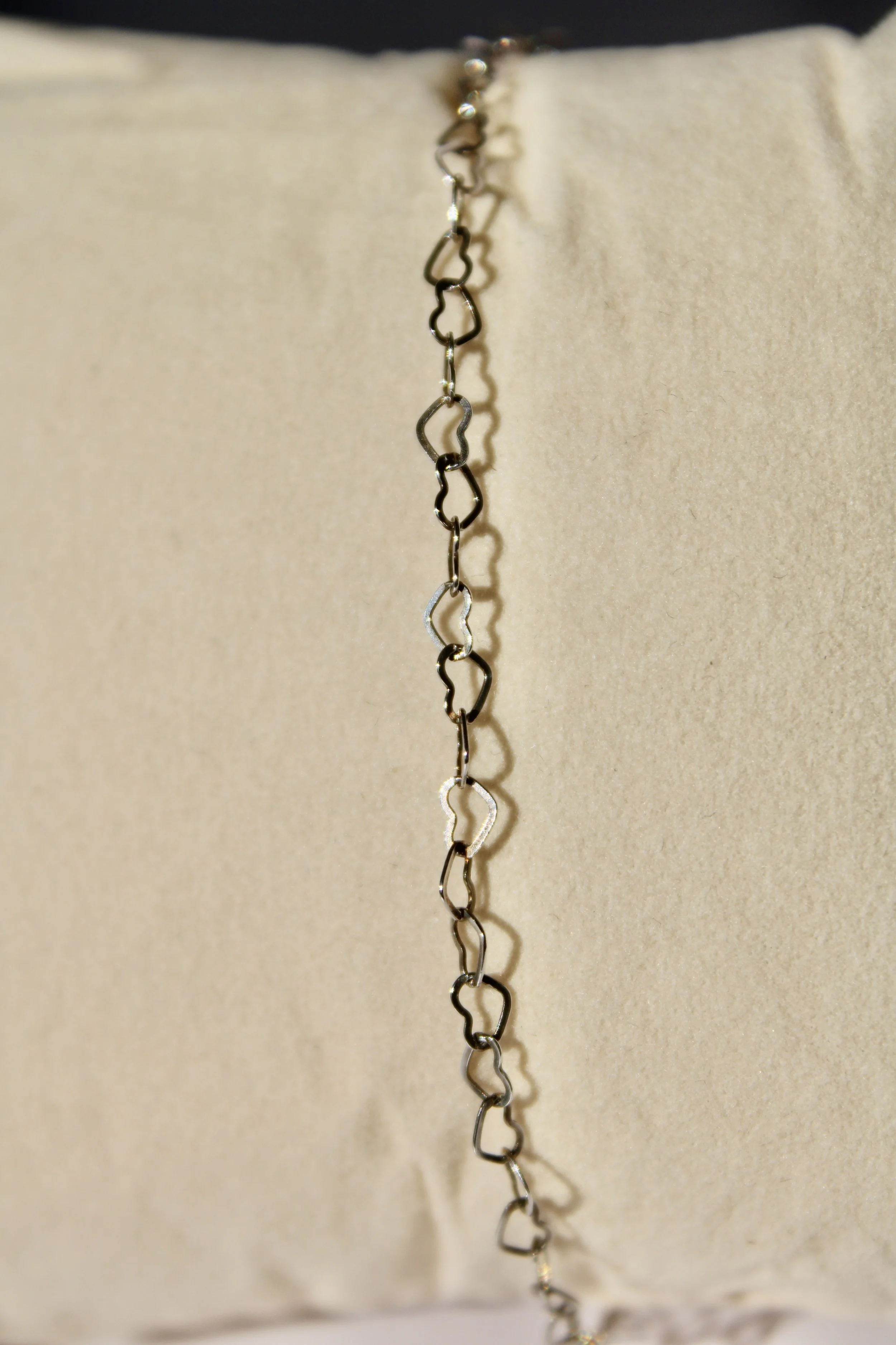 Close-up of a silver chain with interconnected heart-shaped links hanging against a light-colored background.