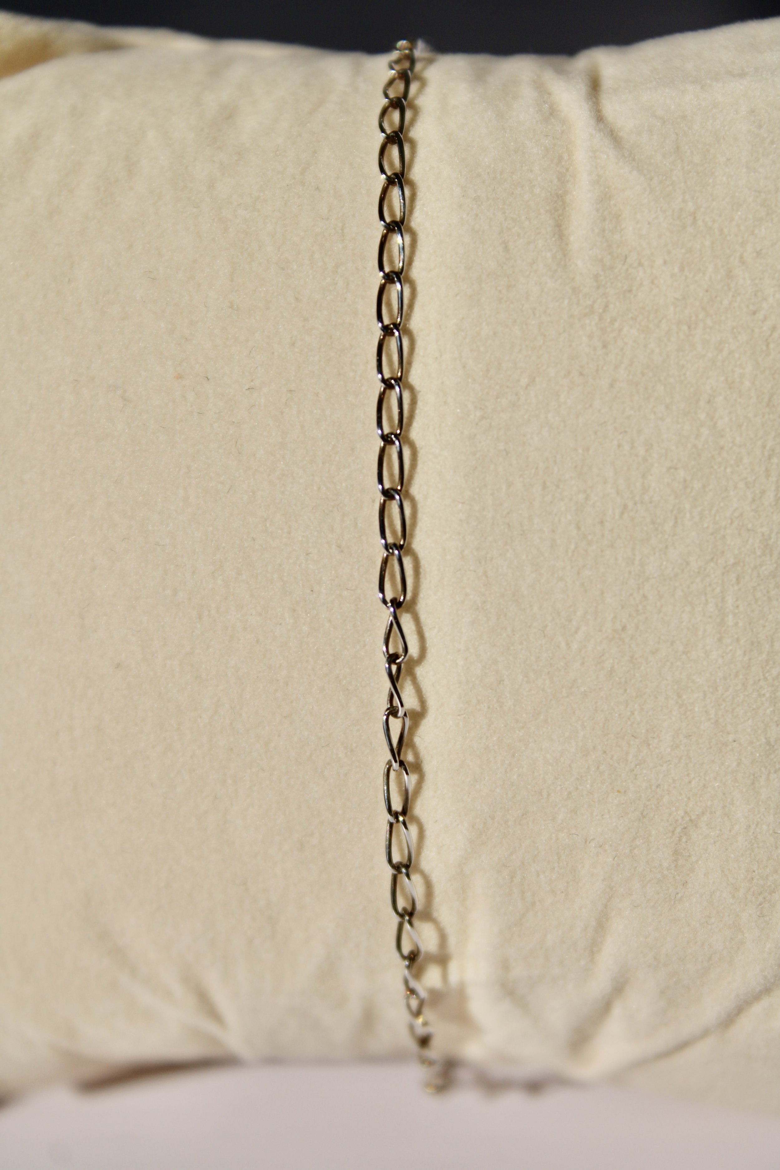 A metal chain hangs vertically in front of a beige fabric background, with a blurred object at the bottom of the image.