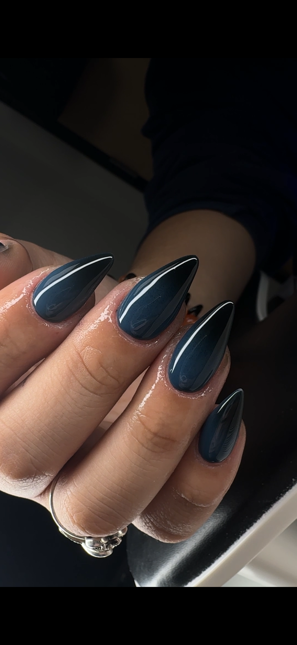 Close-up of a hand with navy blue, glossy, almond-shaped acrylic nails, with a white stripe design, against a dark background.