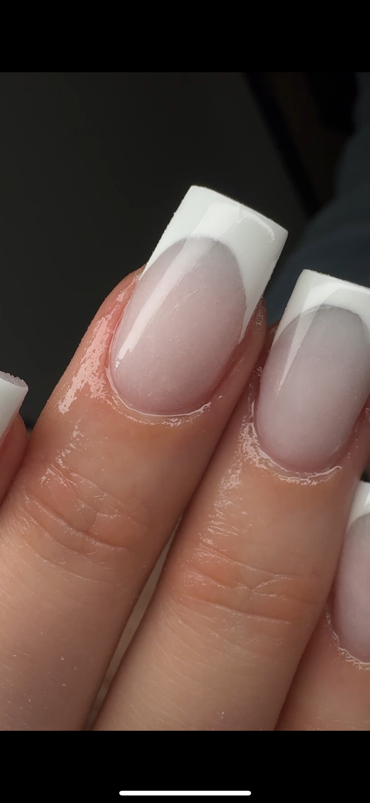 Close-up of manicured fingernails with French tip design on fingers with clear gel polish and shiny finish.