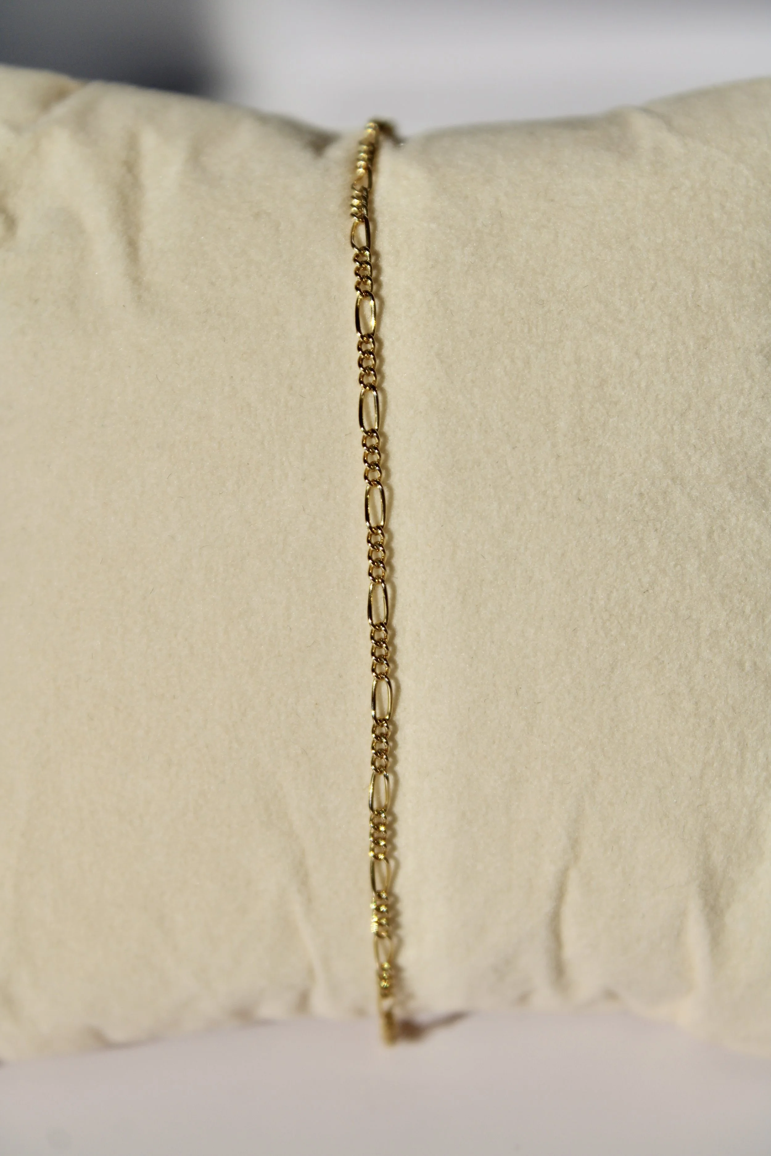 Gold chain necklace hanging on a beige fabric pillow display.