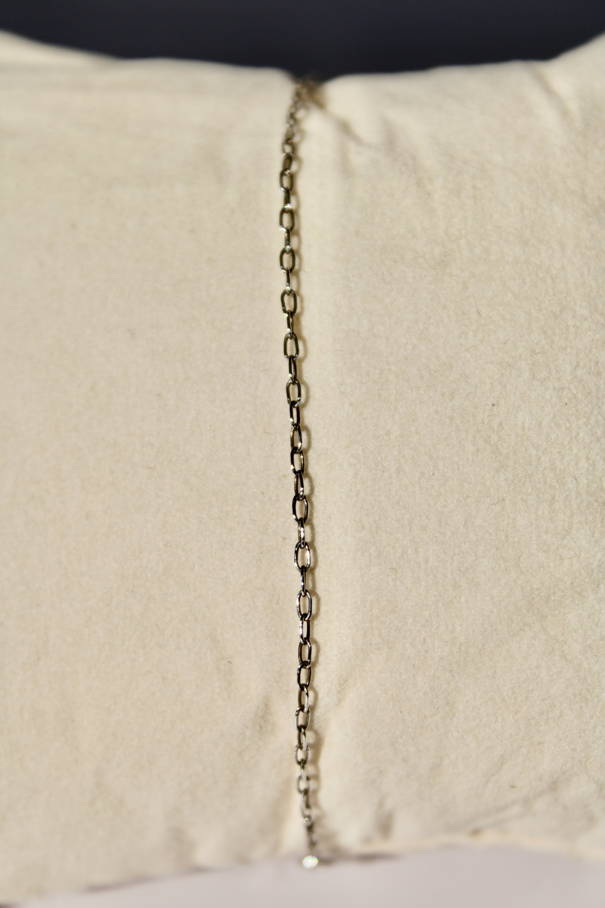 Close-up of a silver chain necklace hanging against a beige textured fabric background.