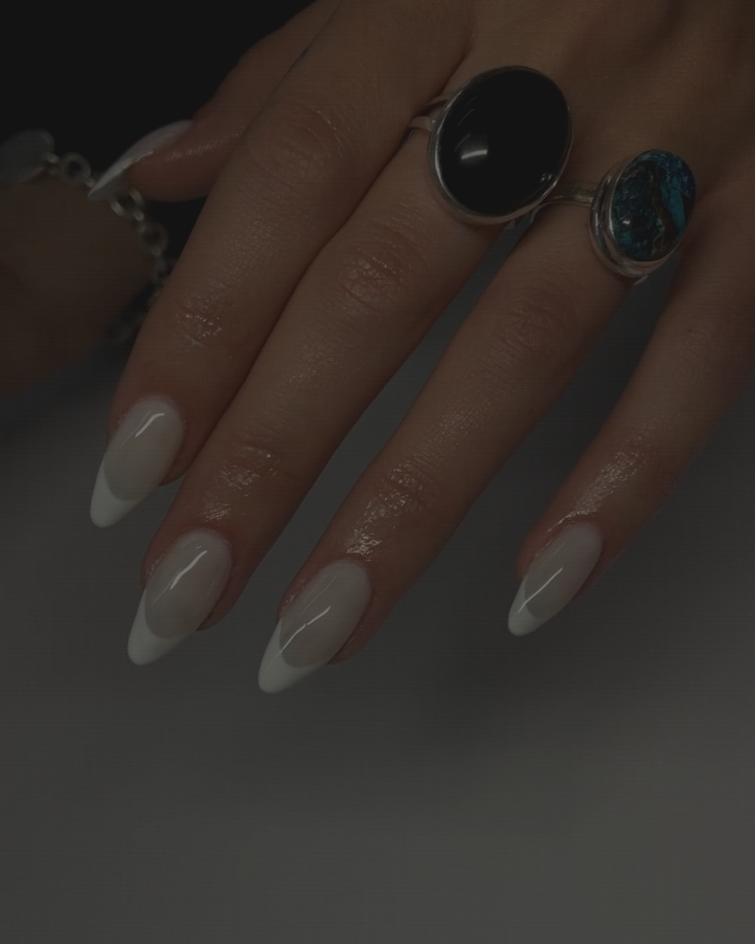 Close-up of a hand with manicured nails and two rings, one silver ring with a large black stone and the other with a turquoise stone.