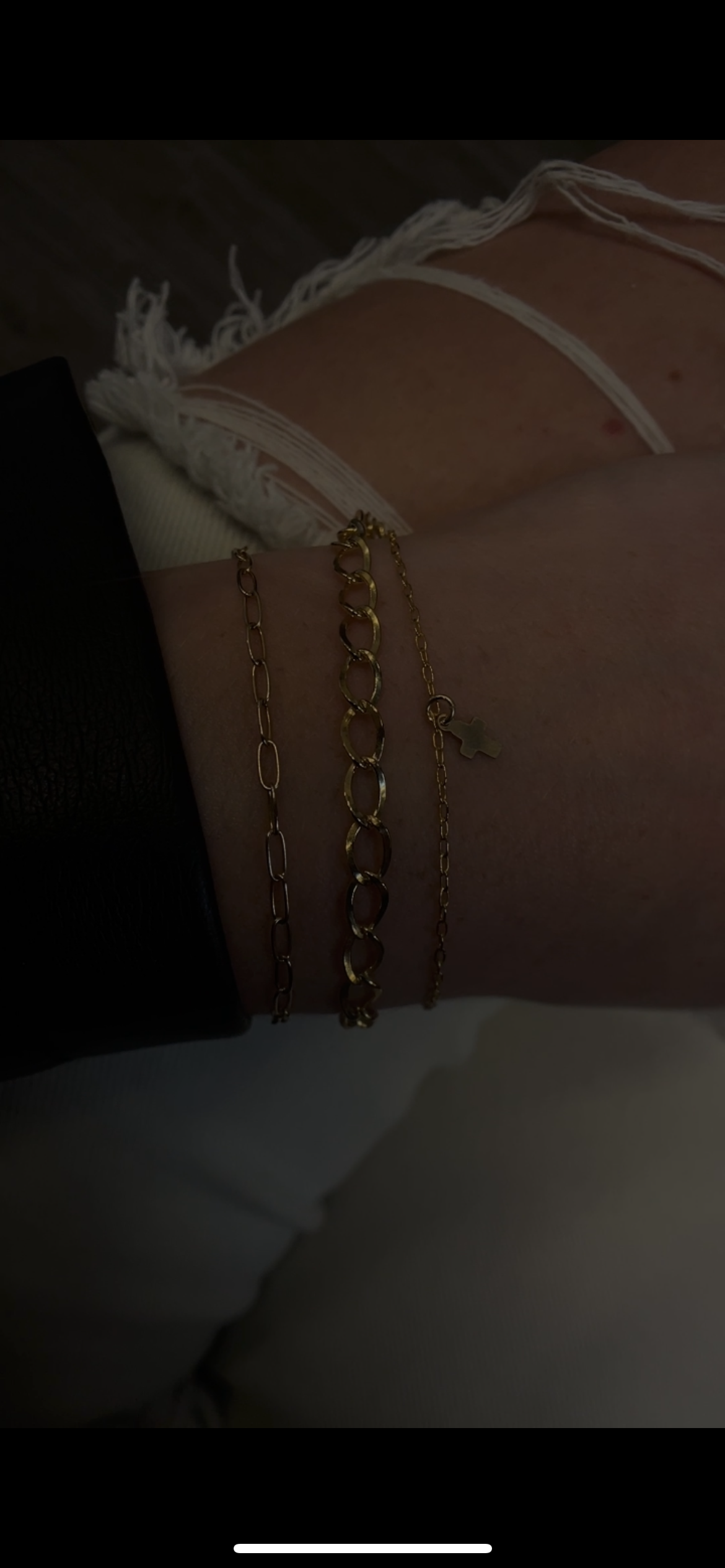 Close-up of a person's wrist with three gold bracelets, with a background showing a person's knee with ripped denim shorts.