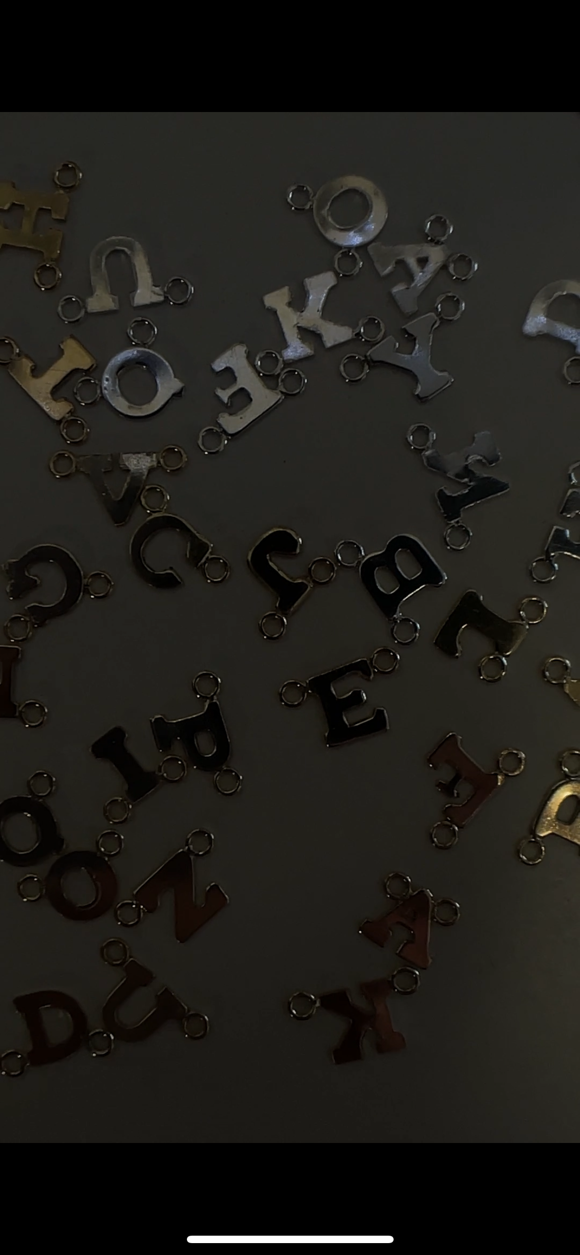 Assorted alphabet charm pendants scattered on a dark surface.