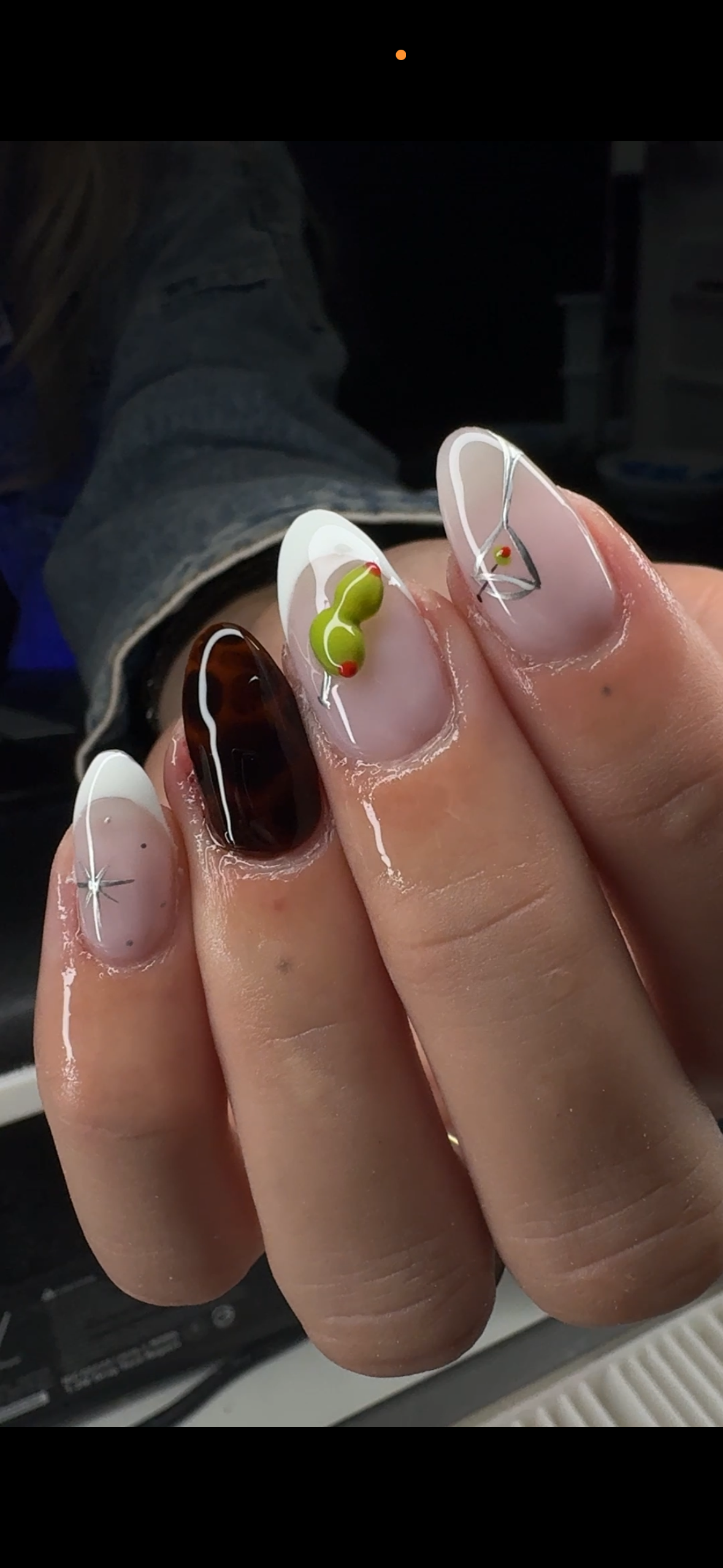 Close-up of a person's hand displaying decorated acrylic nails with artistic 3D designs, including a ladybug, a shiny dark brown nail, and star-like accents.